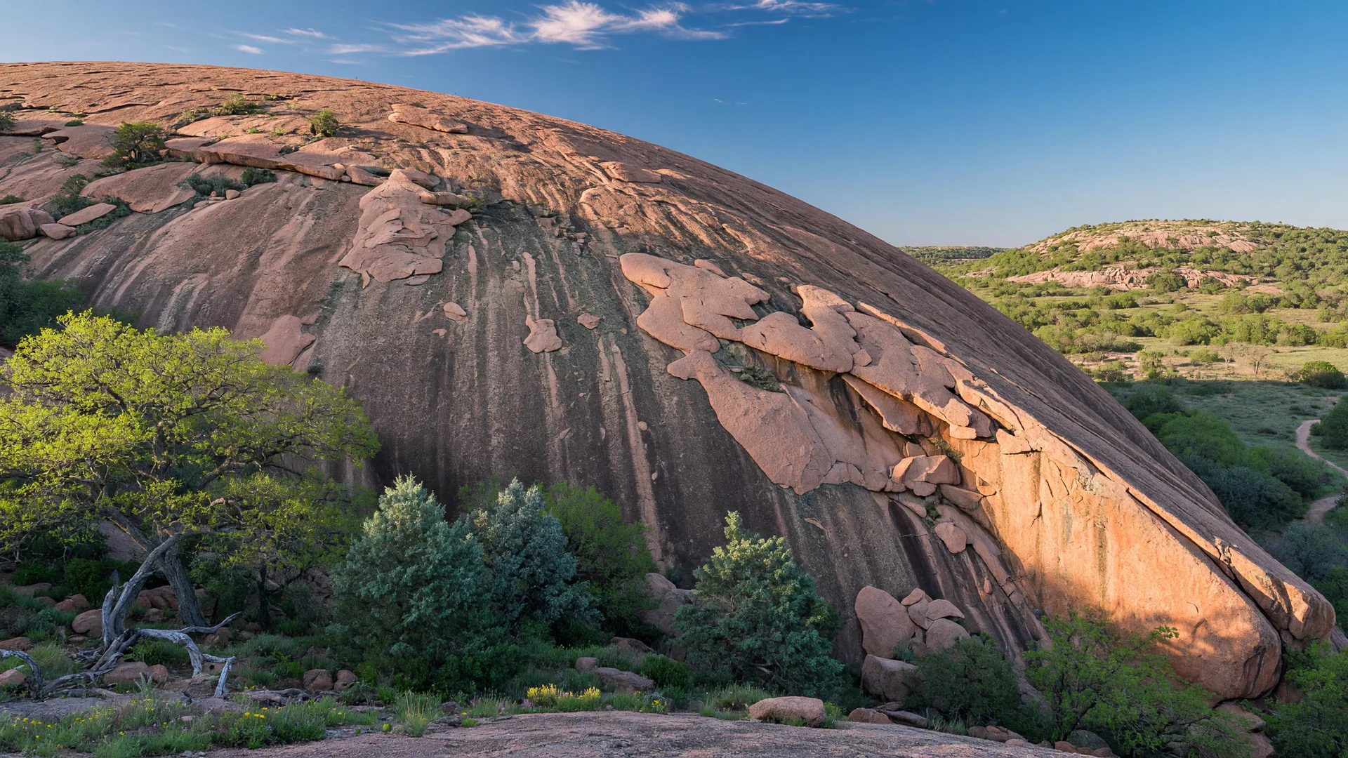 Enchanted Rock, the massive pink granite dome rising above the Texas Hill Country, framed by live oaks and junipers under a blue sky