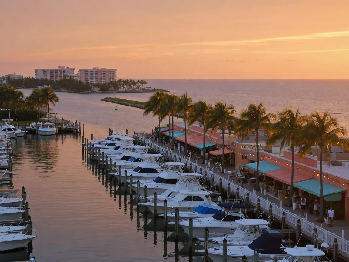 The Riviera Beach marina village at golden hour, docks of white boats and waterfront restaurants with the ocean beyond