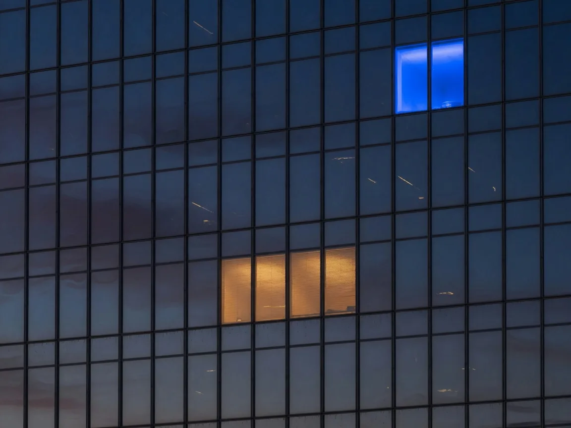Glass skyscraper facade at dusk with one lit blue window