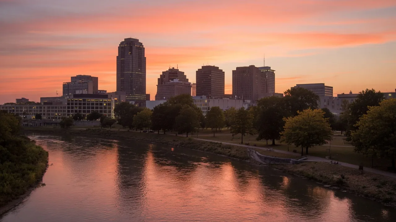 The Dayton Ohio downtown skyline at golden hour reflected in the Great Miami River with warm sunset tones and historic buildings