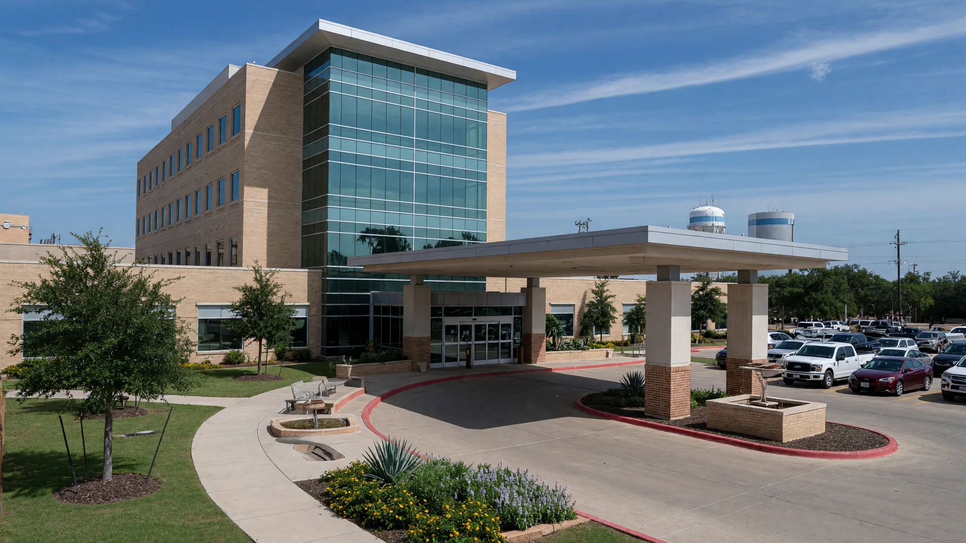 A modern glass-and-brick regional hospital entrance in a small Texas town with a covered drop-off canopy and landscaped walkways