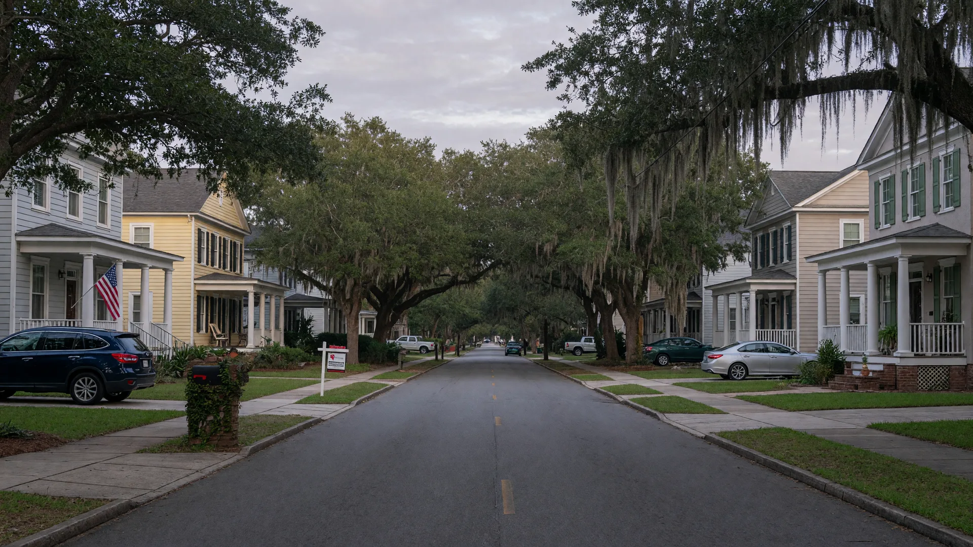 A quiet suburban street of front-porch homes and live oaks in the Charleston Lowcountry in soft early-morning light