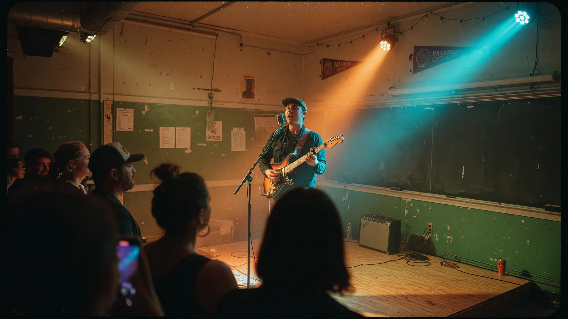 A guitarist performing on a low stage in an intimate Pasadena listening room under warm amber stage lights