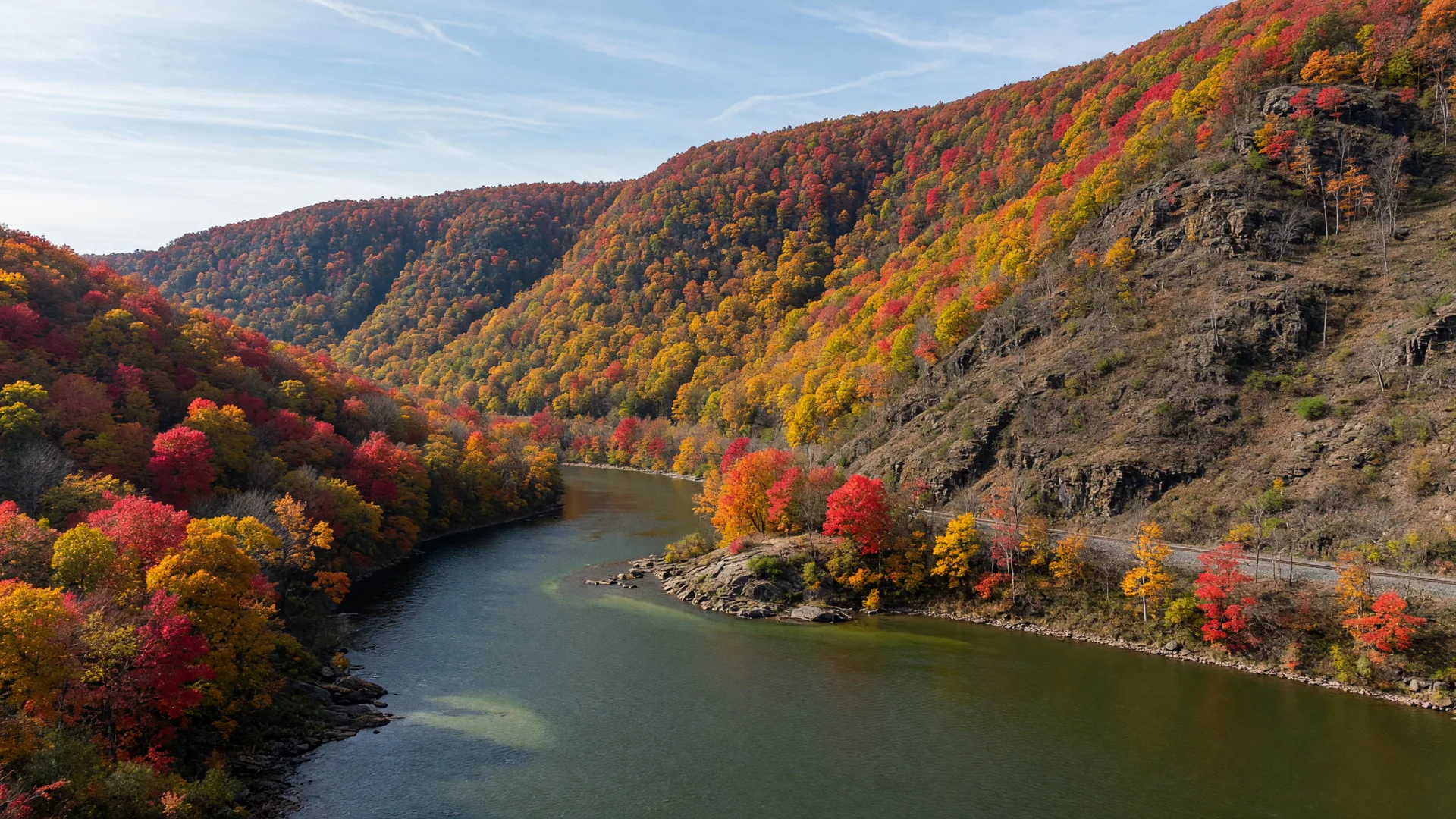 The Lehigh River curving through the Lehigh Gap in the Kittatinny Ridge in late October, forested slopes in peak gold, orange, and crimson fall color under a clear autumn sky