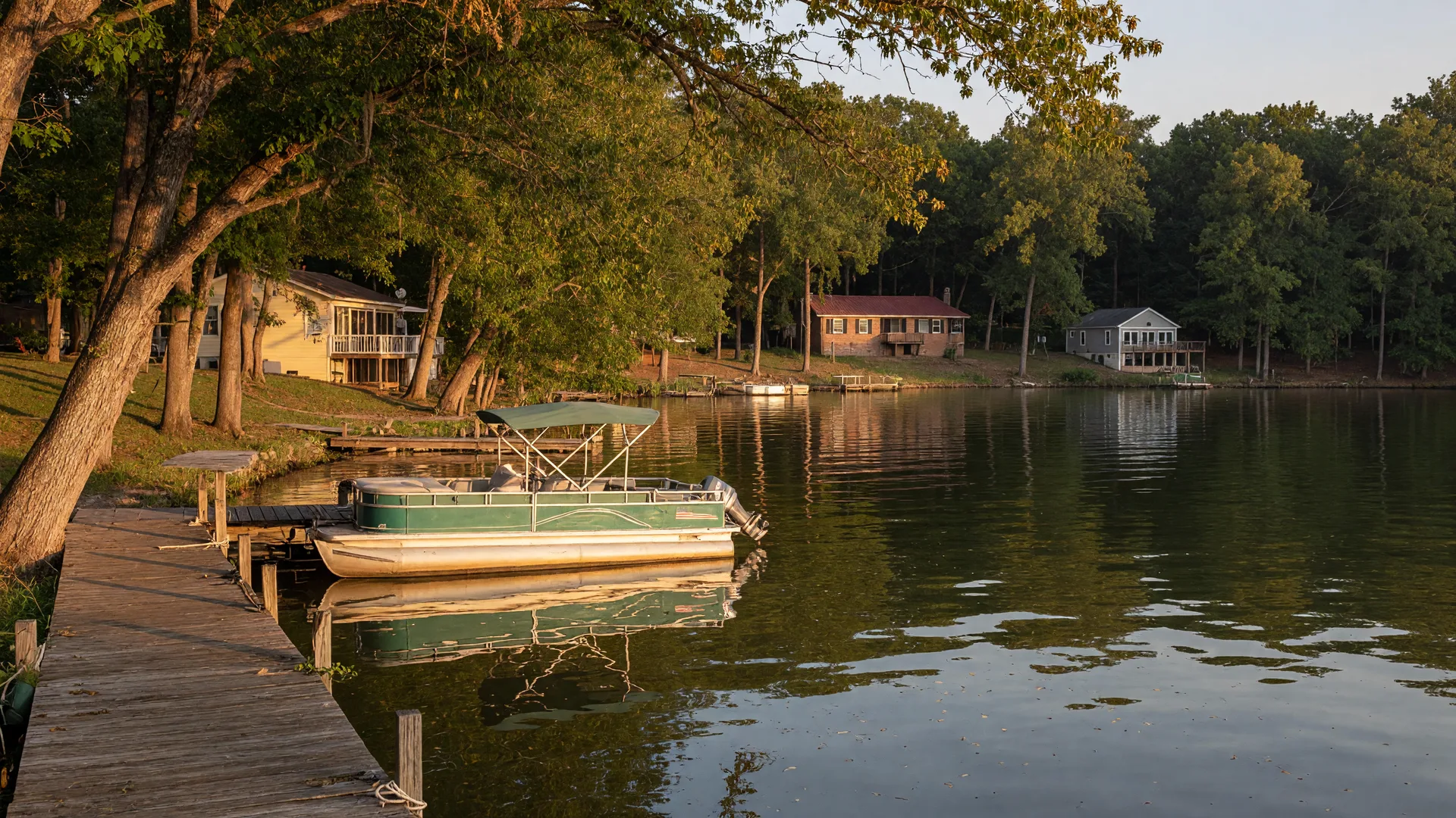 Golden-hour view of a quiet tree-lined cove on Lake Wylie with a wooden dock and moored pontoon boat