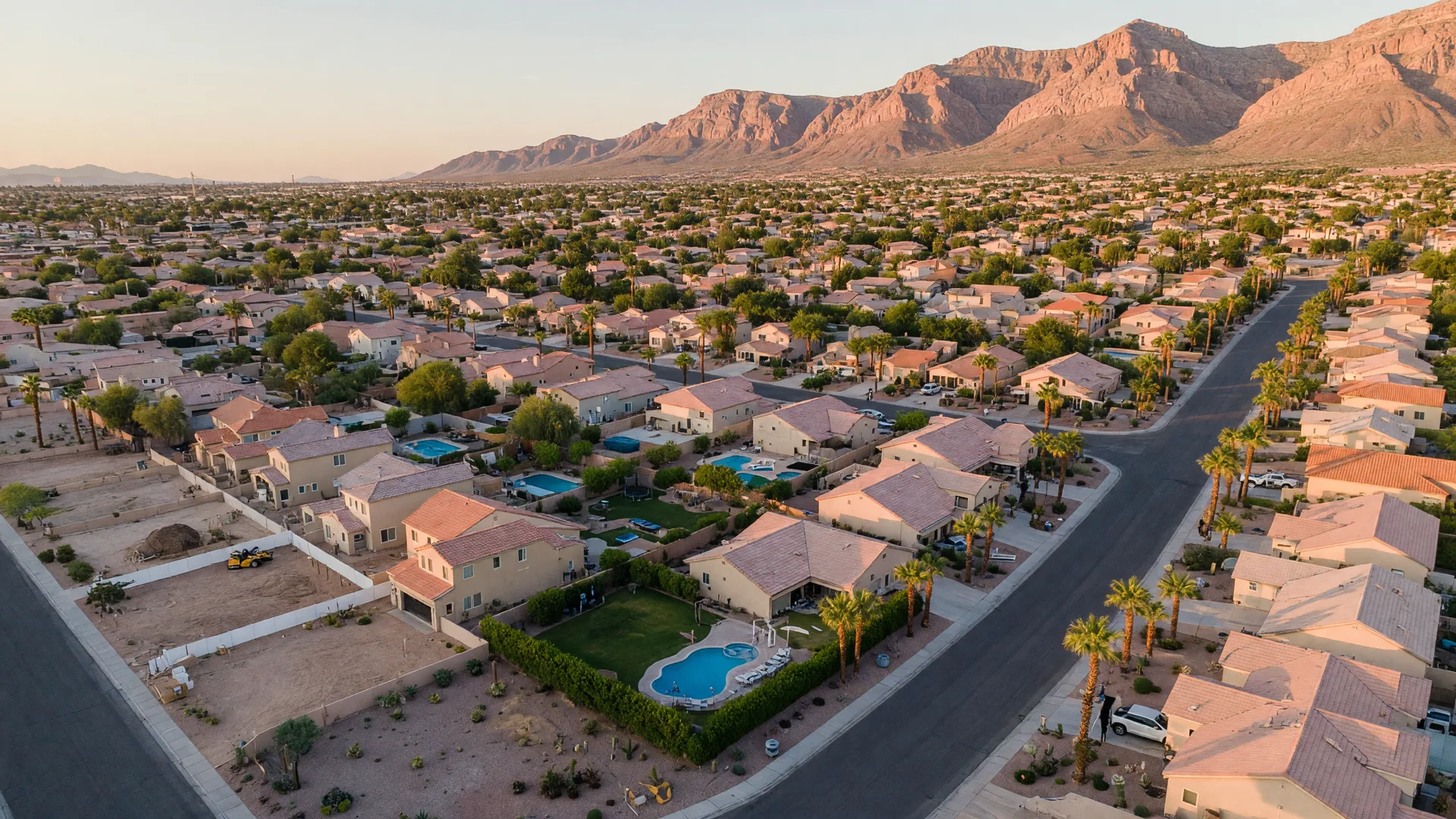 Aerial view of a suburban Las Vegas neighborhood at golden hour with tile-roof homes, palm trees, and mountain views