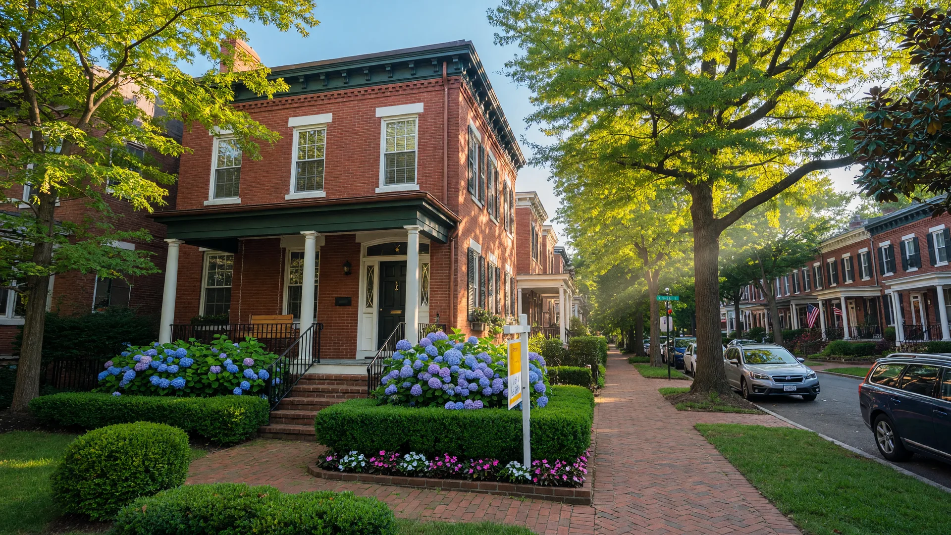 Historic brick row house with a For Sale sign in a leafy Washington DC neighborhood on a late summer morning, with mature trees and a landscaped front yard