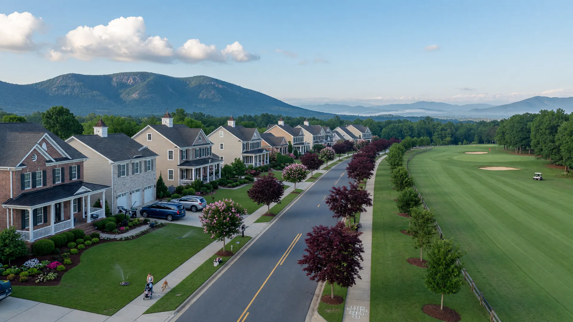A tree-lined street of stately single-family homes in a planned Haymarket, Virginia community, with manicured lawns and a golf fairway beneath the Blue Ridge foothills