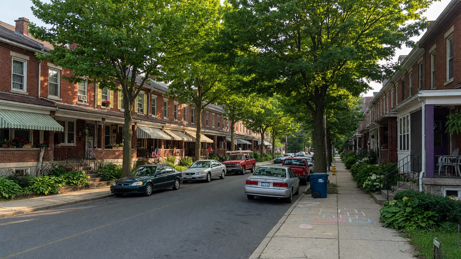 Tree-lined residential street in Darby, Pennsylvania with historic 1920s row homes and twin houses on a sunny afternoon