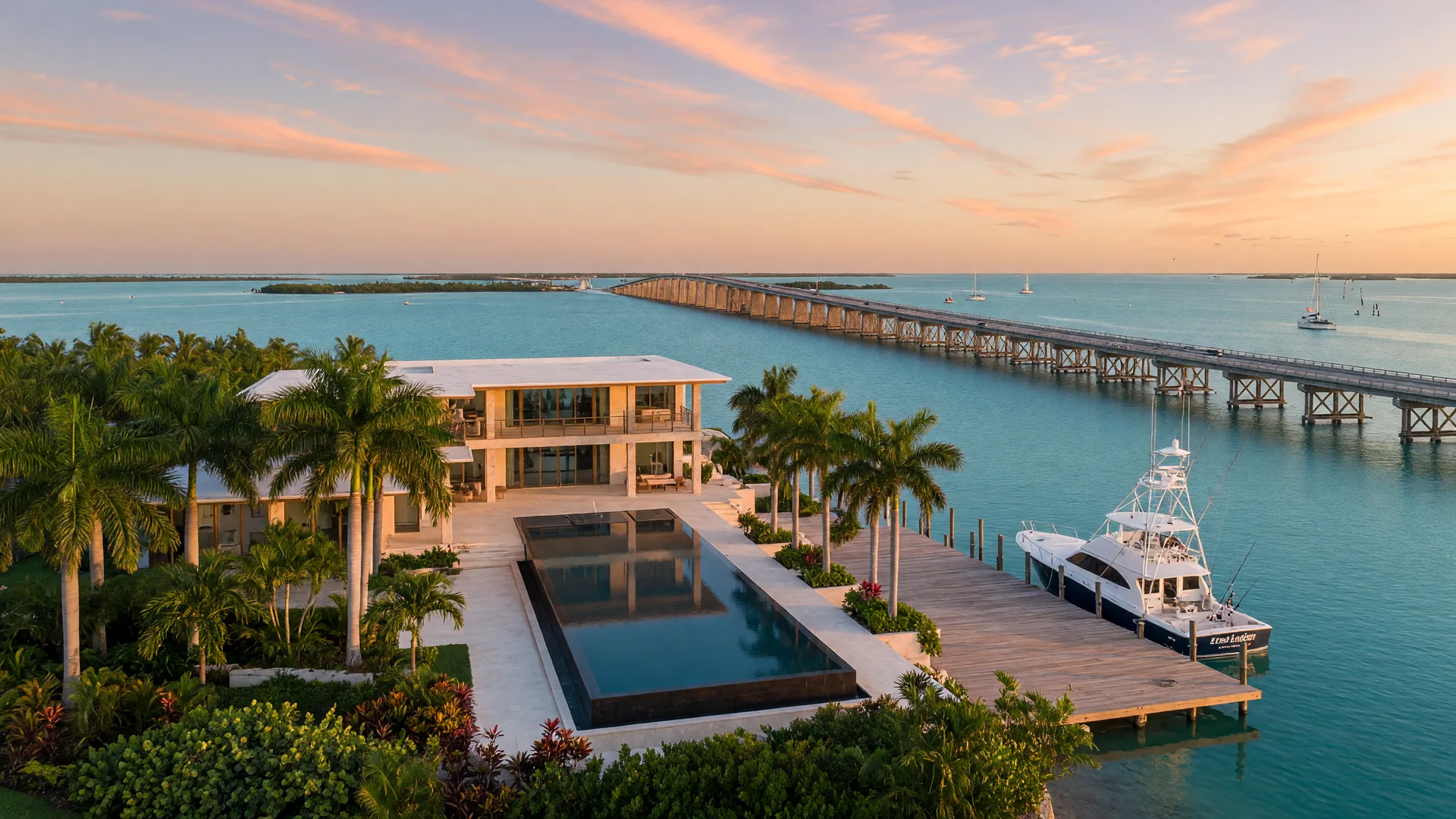 Luxury bayfront estate in Marathon at sunrise with infinity pool overlooking turquoise water, private dock with sportfishing yacht, Seven Mile Bridge in distance, tropical landscaping