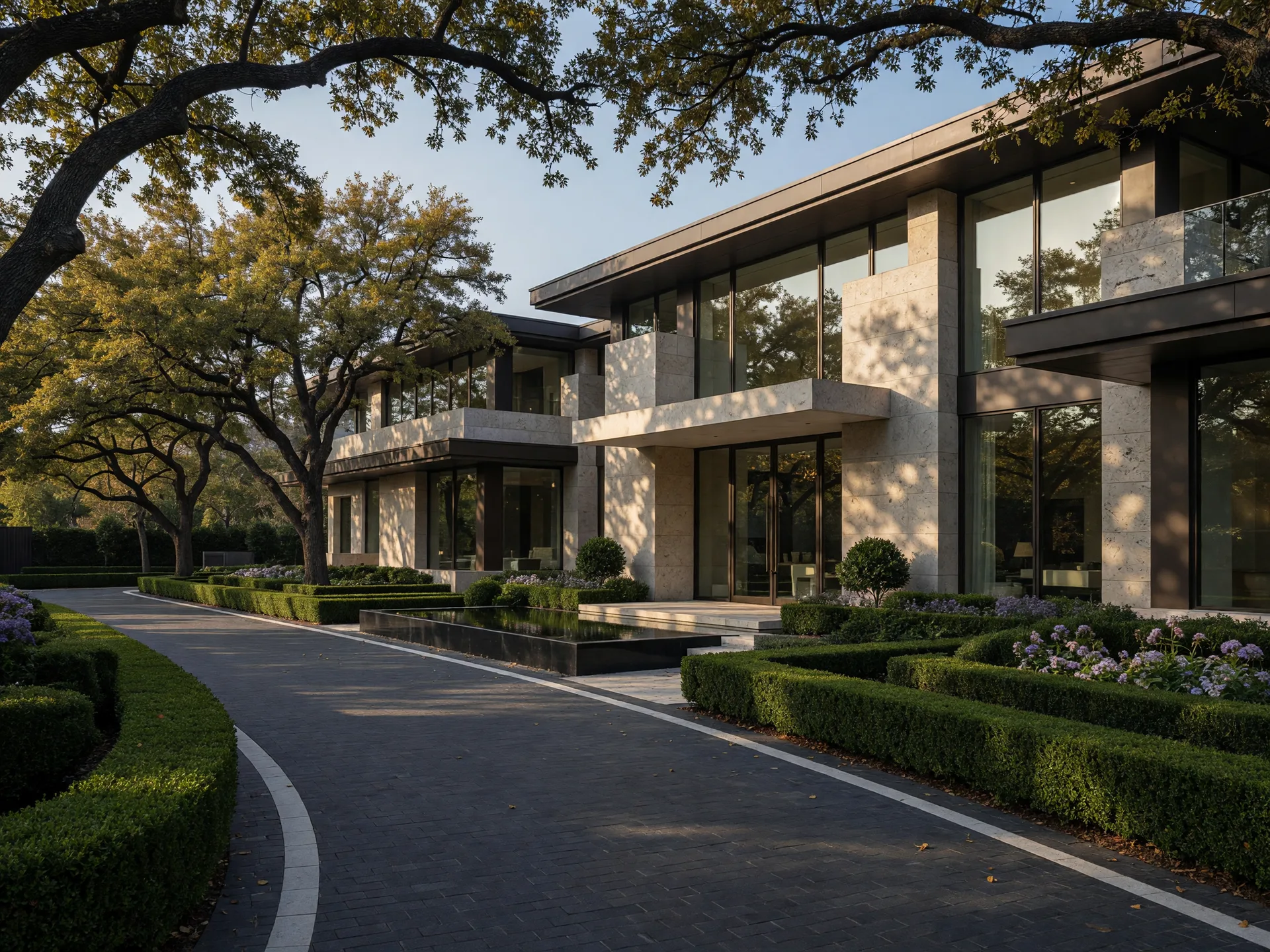 Grand Dallas luxury estate at golden late-afternoon light with a tree-lined drive, limestone and glass architecture, and mature oak landscaping