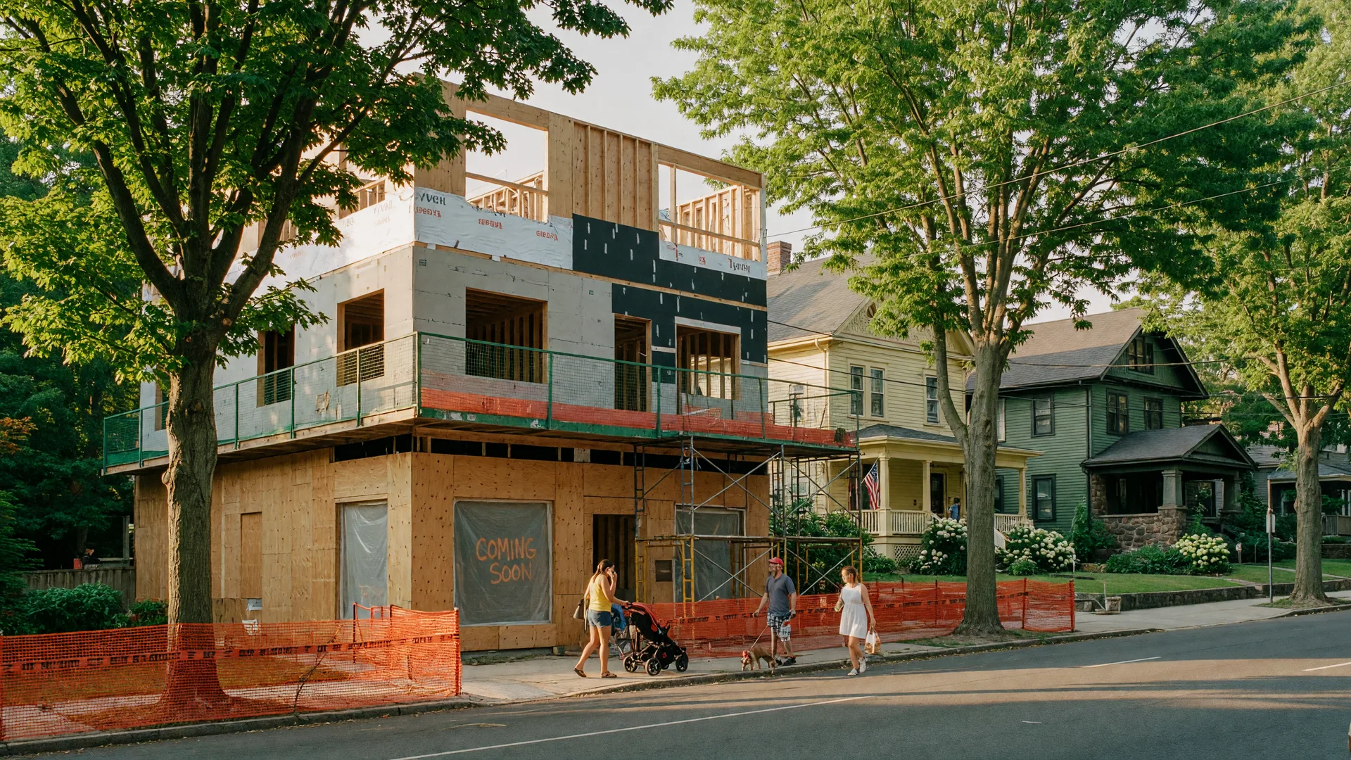 A mixed-use building under construction on a tree-lined street in Montclair NJ with scaffolding and pedestrians
