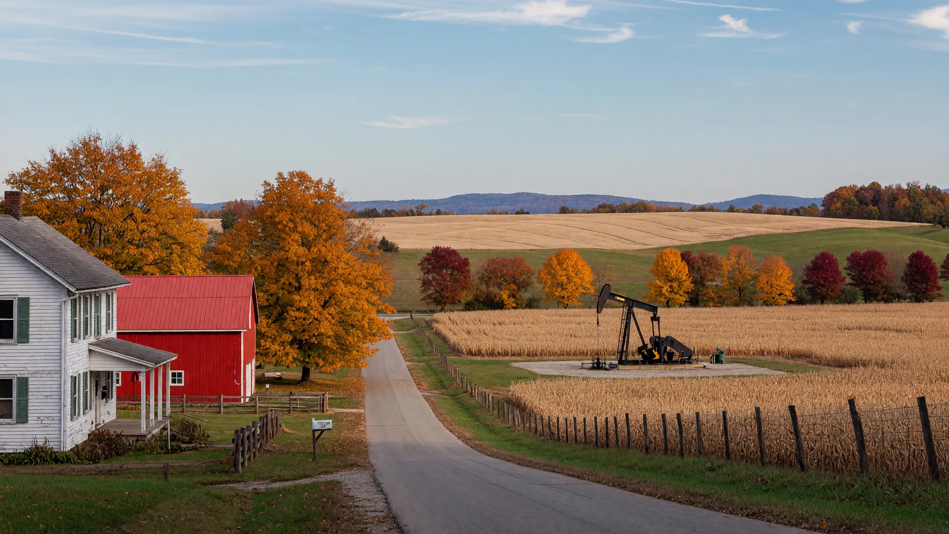 Rolling farmland in eastern Ohio on a clear October afternoon, a white farmhouse and red barn near a rural two-lane road in the foreground and a natural gas wellhead pump on a distant pad, with autumn trees turning orange and gold along the fence line