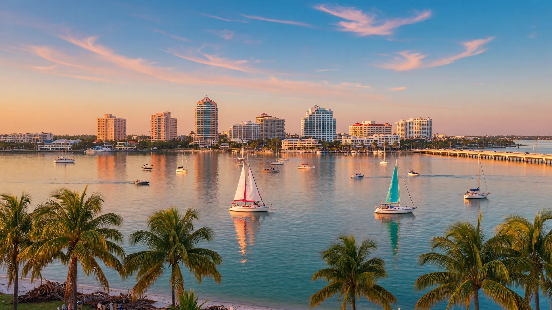 Sarasota Bay and downtown skyline at golden hour with sailboats and palm trees