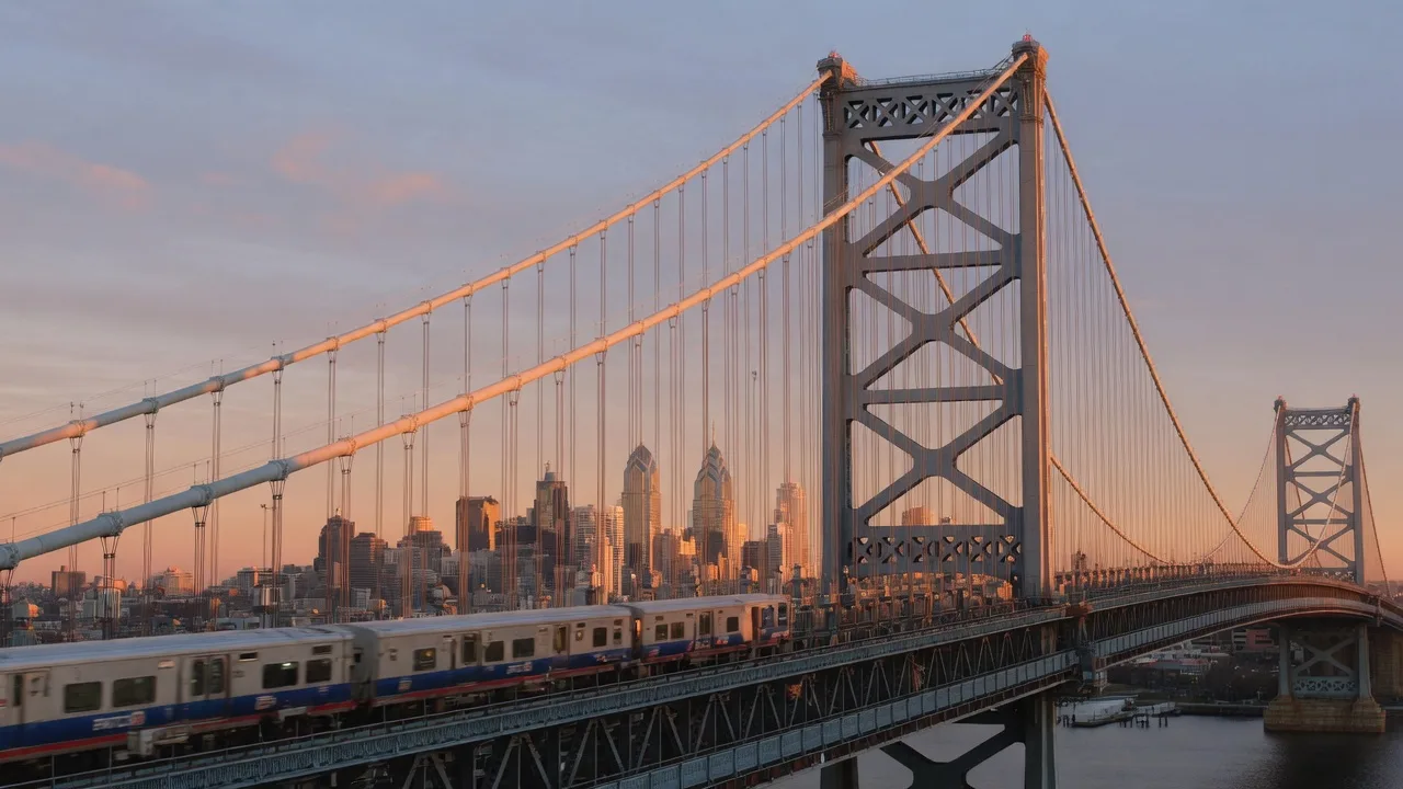 Benjamin Franklin Bridge connecting South Jersey to Philadelphia at sunrise with a PATCO train crossing