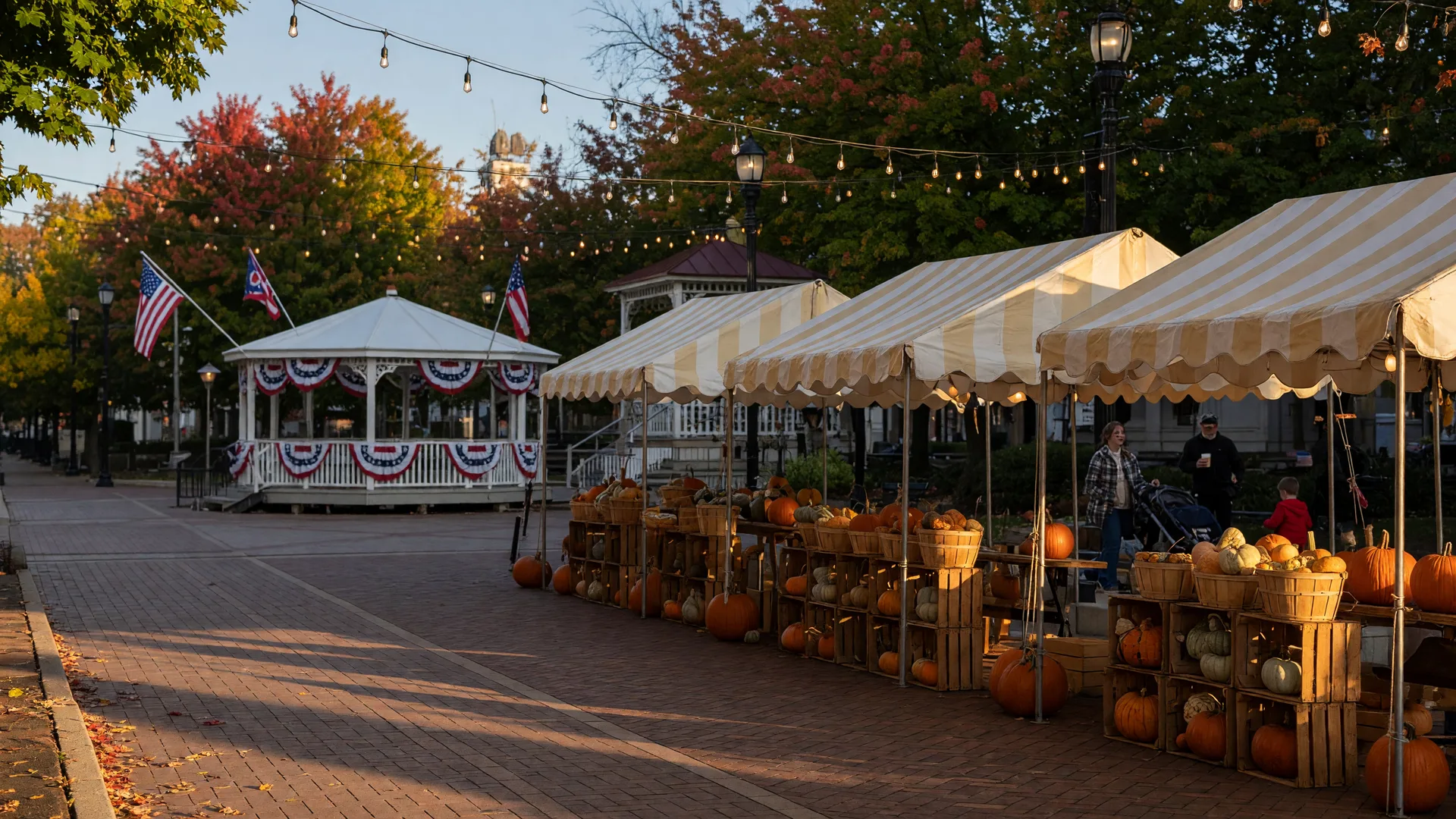 A crisp late-September afternoon on a historic Ohio town square with festival vendor canopies, stacked pumpkins, glowing string lights, a flag-bedecked band shell, and maples turning red and gold