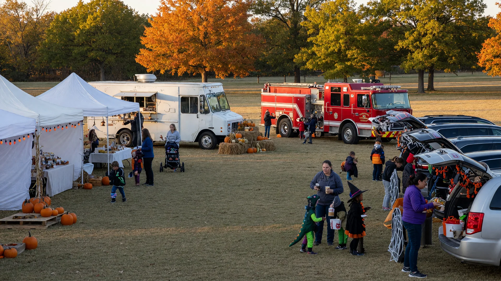 Free community fall festival at O'Brien Park in north Tulsa with vendor tents, food trucks, a trunk-or-treat area, and families in costume under golden October light