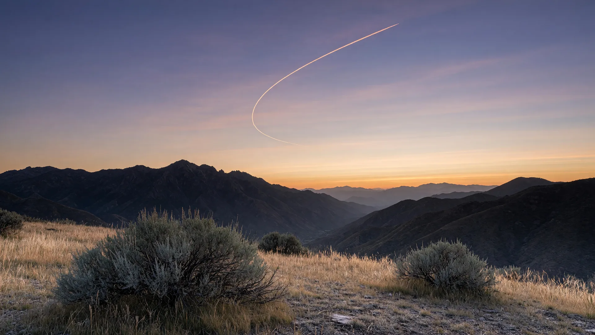 Dawn over the Wasatch Mountains with a single jet contrail arcing across the sky