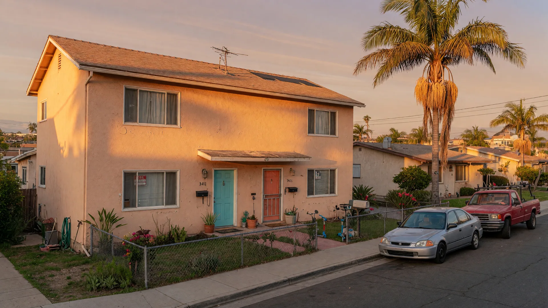 A classic San Diego duplex on a sunny residential street with separate front doors and a small yard, golden-hour light on the stucco facade