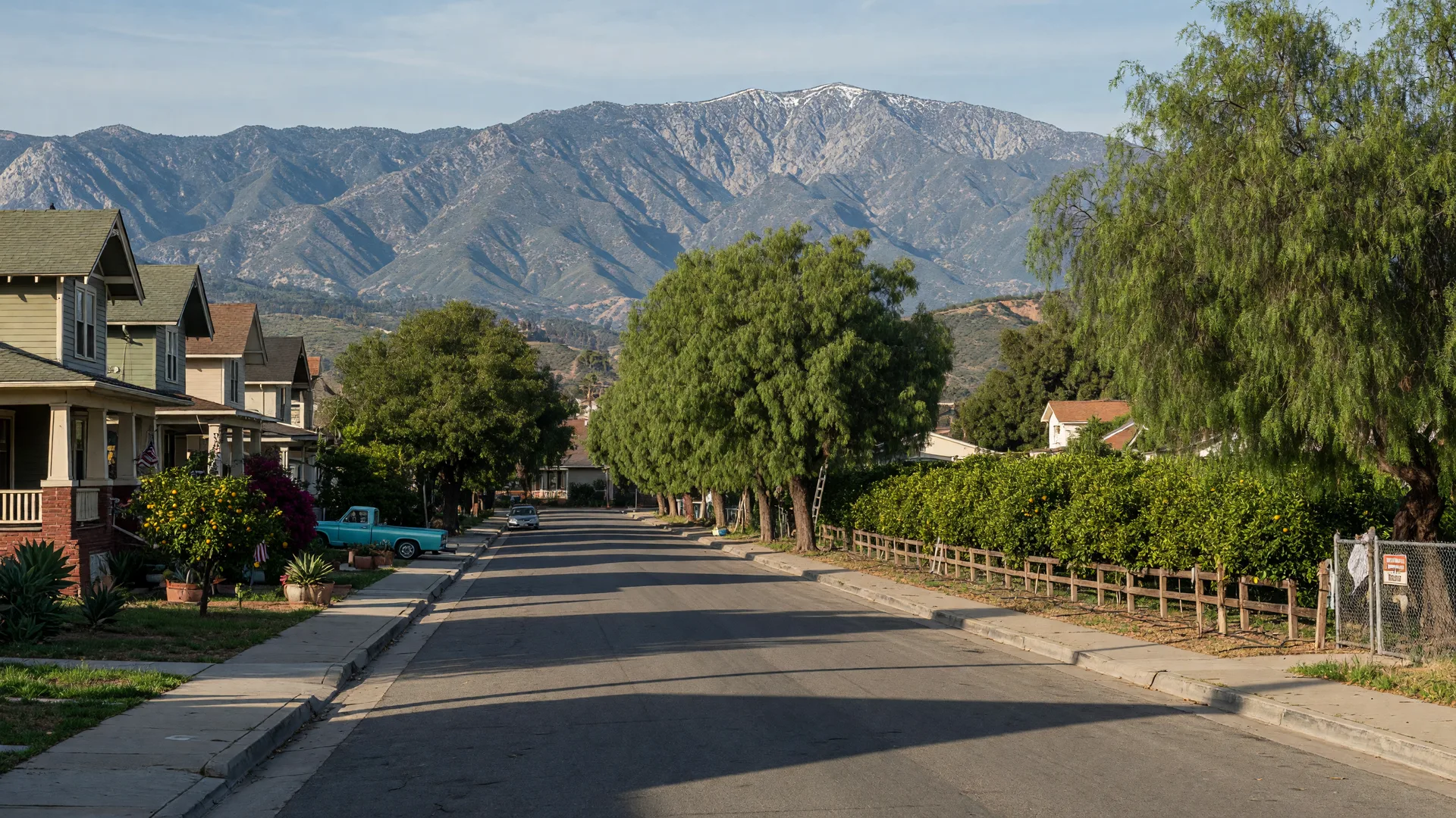 Sunny Upland residential street with older craftsman homes, mature trees and lemon groves, and the San Gabriel Mountains behind