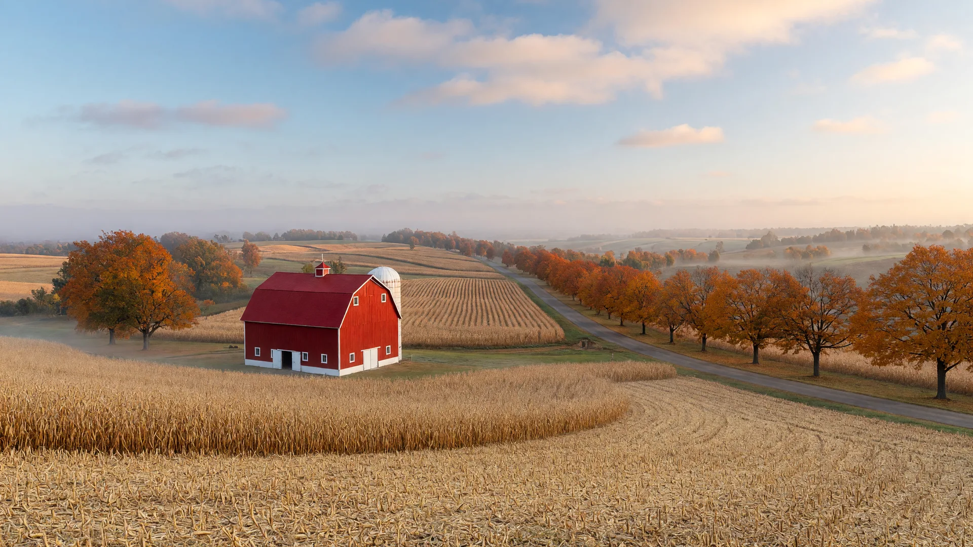 Rolling farmland and a red barn under a bright autumn sky