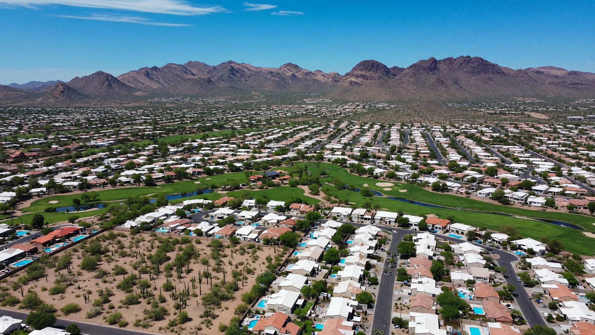 Aerial view of the Phoenix metro valley spreading toward desert mountains on a clear sunny day
