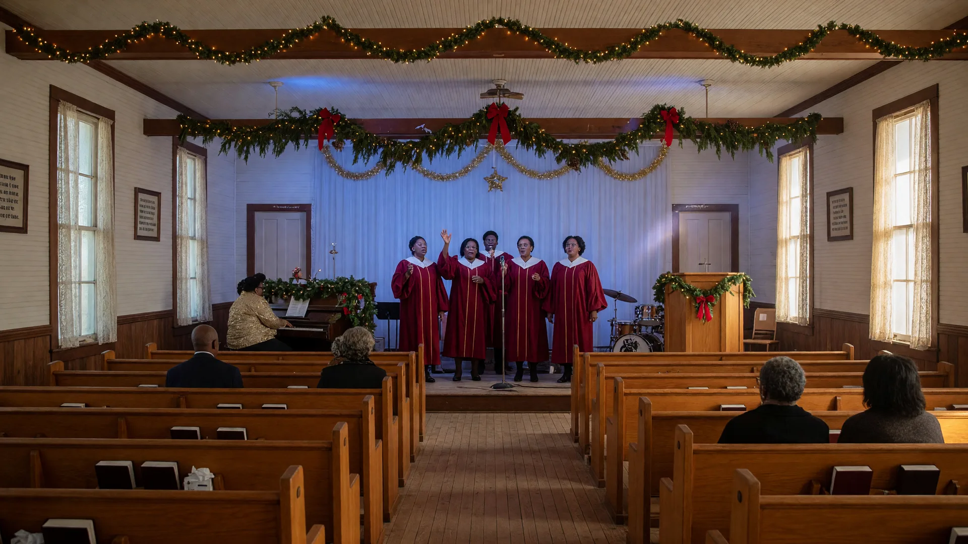 A Southern gospel Christmas concert stage in a small Texas country church, dressed in warm white Christmas lights and garland under soft blue and gold lighting