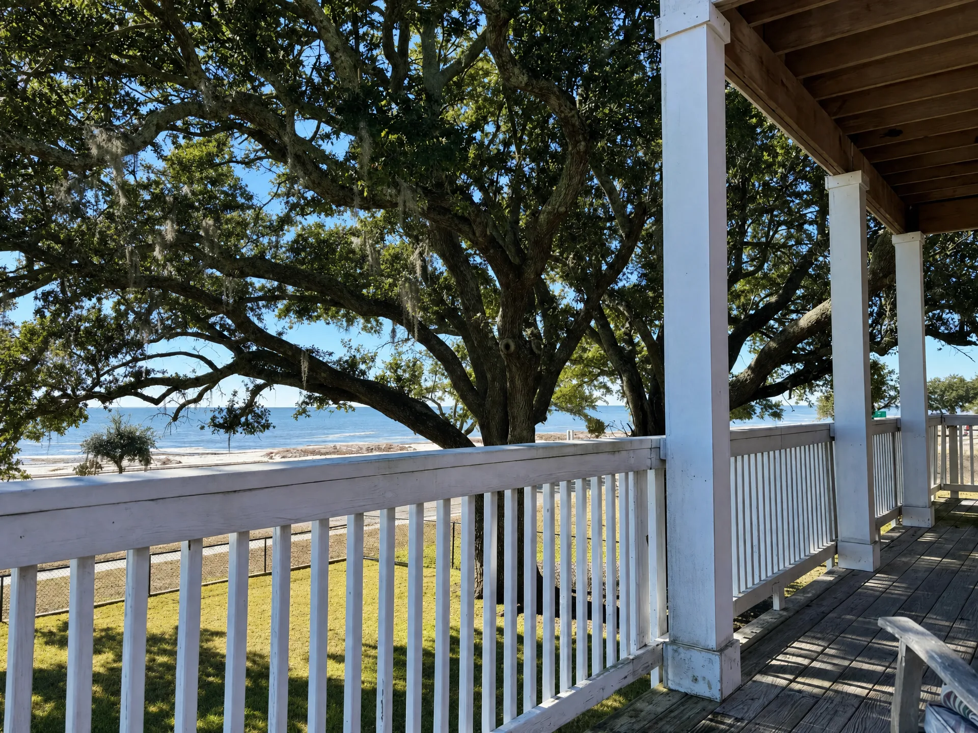 View of a peaceful coastal landscape with a large oak tree and the ocean visible from a wooden residential porch