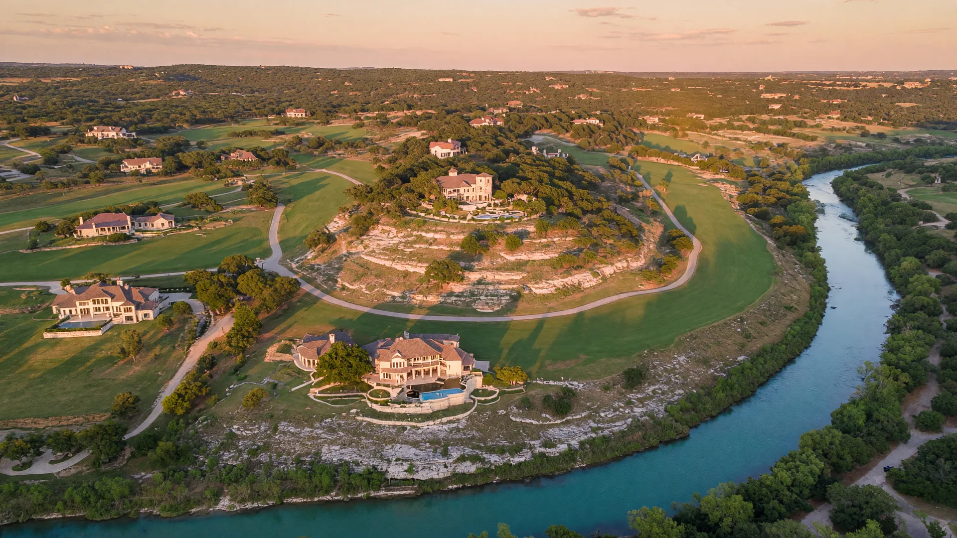 Aerial drone view showing a golf course winding through Hill Country terrain with a river corridor in the distance. Illustrative image; not a photograph of Cordillera Ranch.
