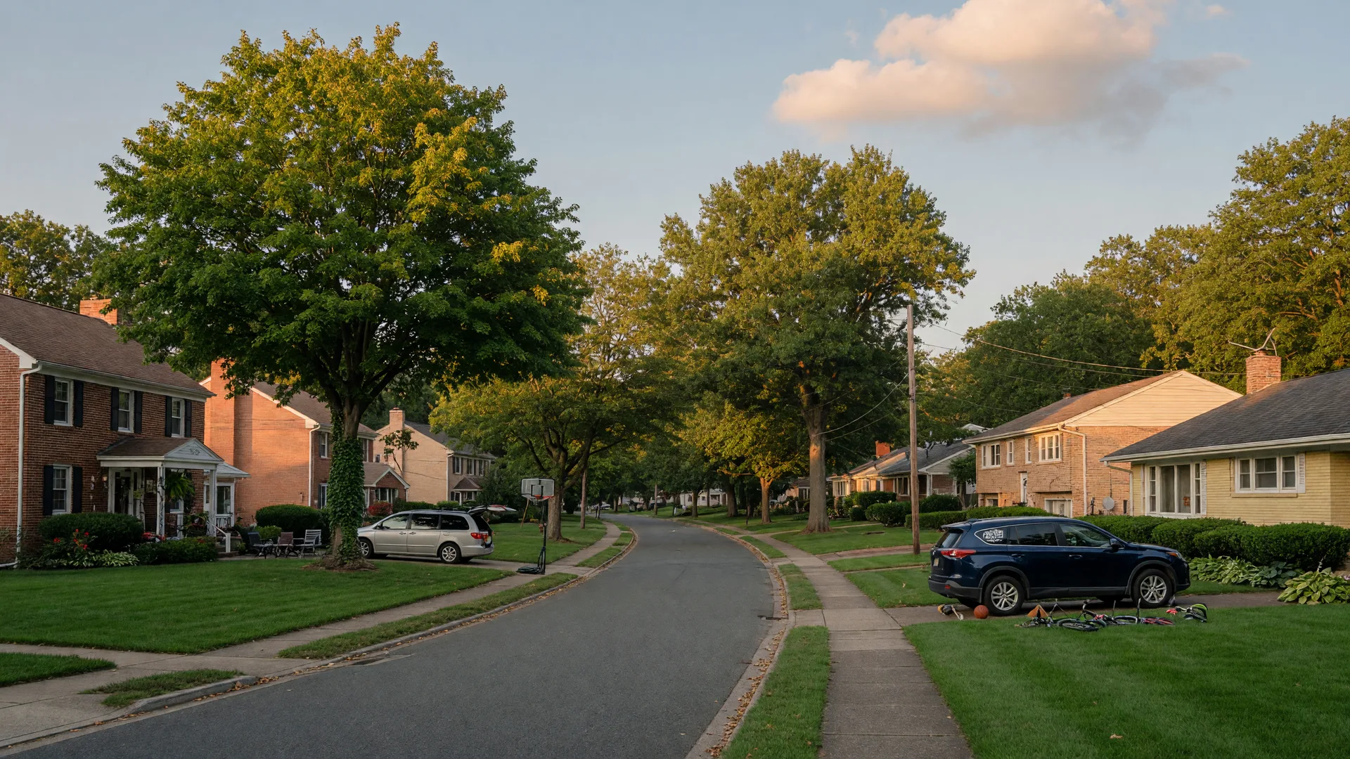 Tree-lined street of larger family homes in a South Jersey suburb at golden hour, with mature trees and deep green lawns