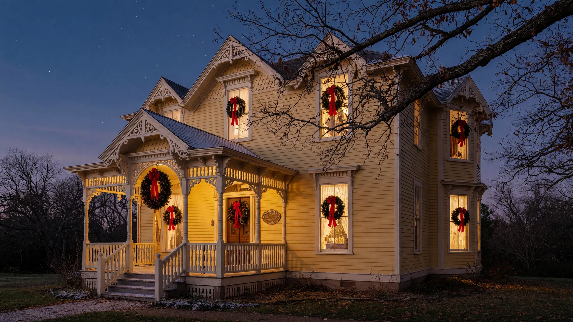 A yellow-siding Victorian house dressed for Christmas at twilight with evergreen wreaths, red bows, and warmly glowing windows