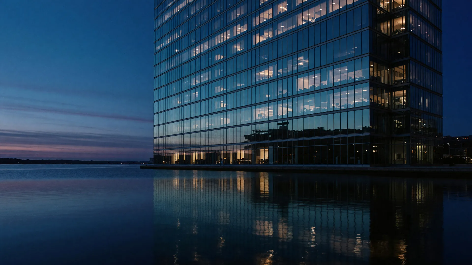 Glass high-rise towers glowing at blue hour across calm water