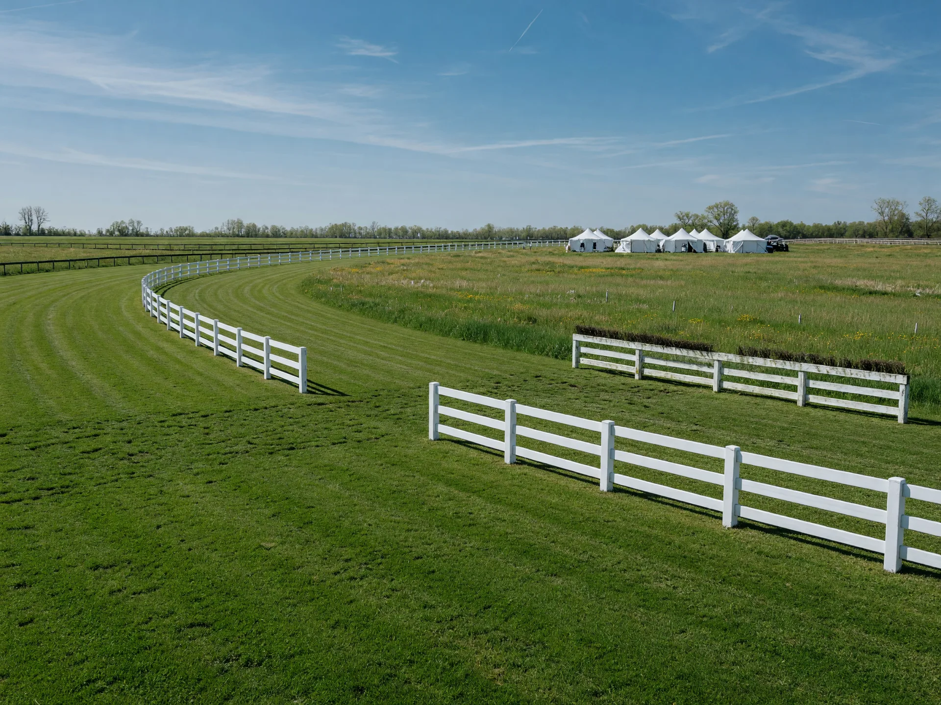 The Aiken steeplechase course on a spring afternoon with white timber fences and distant spectator tents