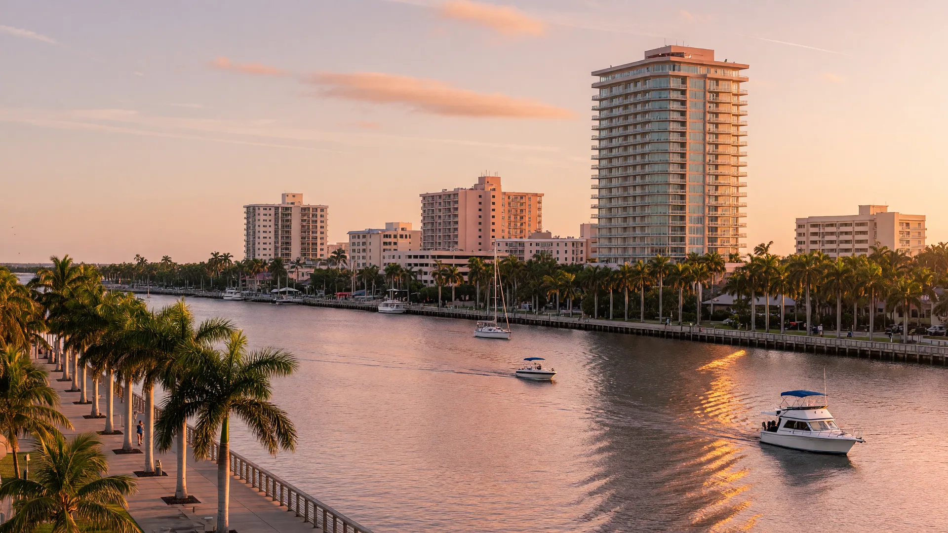 Golden-hour view of downtown Fort Myers, Florida with the Caloosahatchee River, boats, and the downtown skyline rising behind palm trees