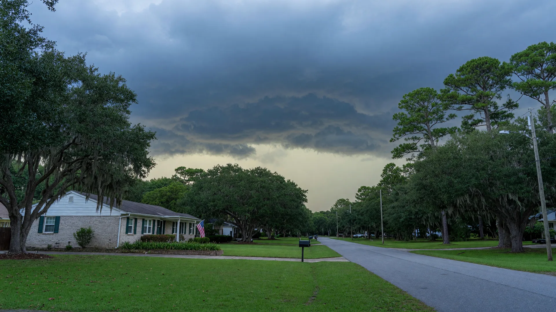A quiet suburban street in the Charleston Tri-County with a single-level brick and siding home and storm clouds gathering on the horizon