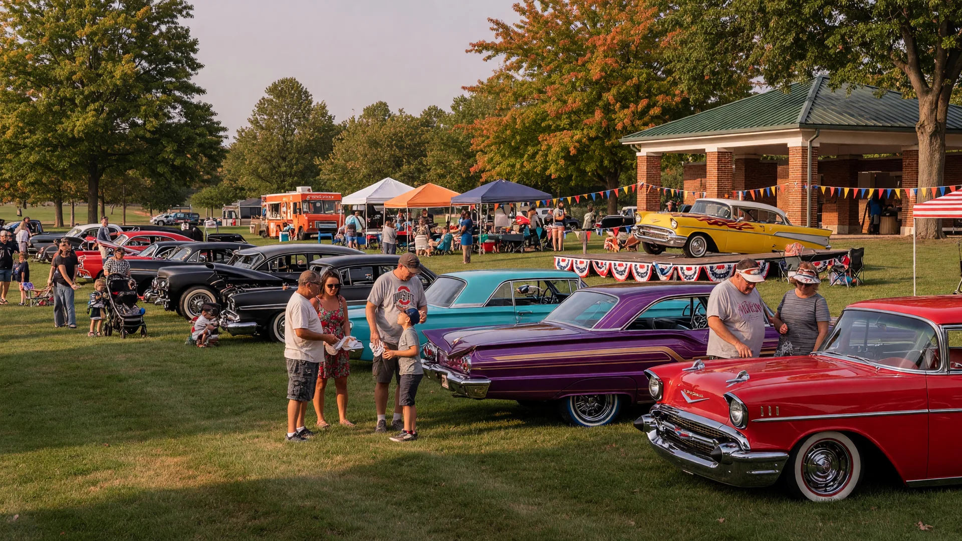 Polished classic cars lined up on the lawn of Memorial Park with families strolling between them and food truck tents in the background on a sunny September afternoon