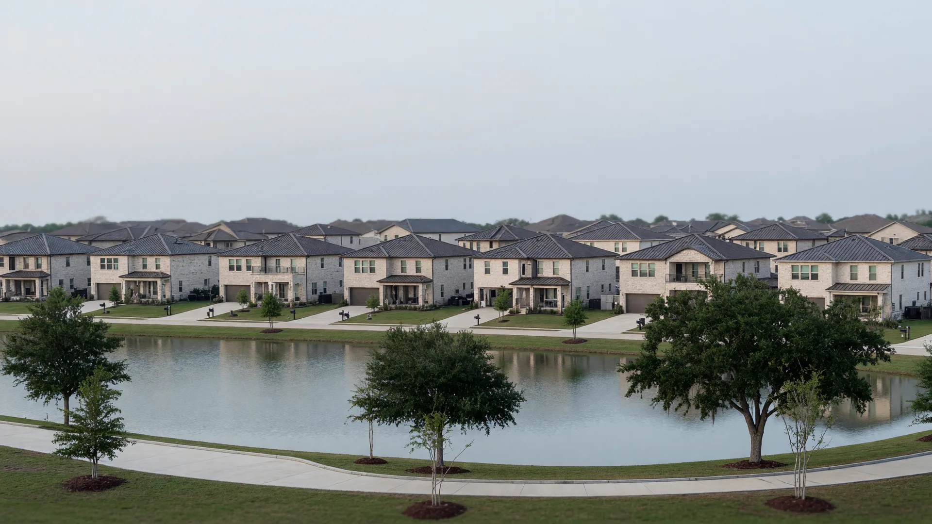 A calm lake with a walking trail and pale-brick homes along the bank in a Texas master-planned community