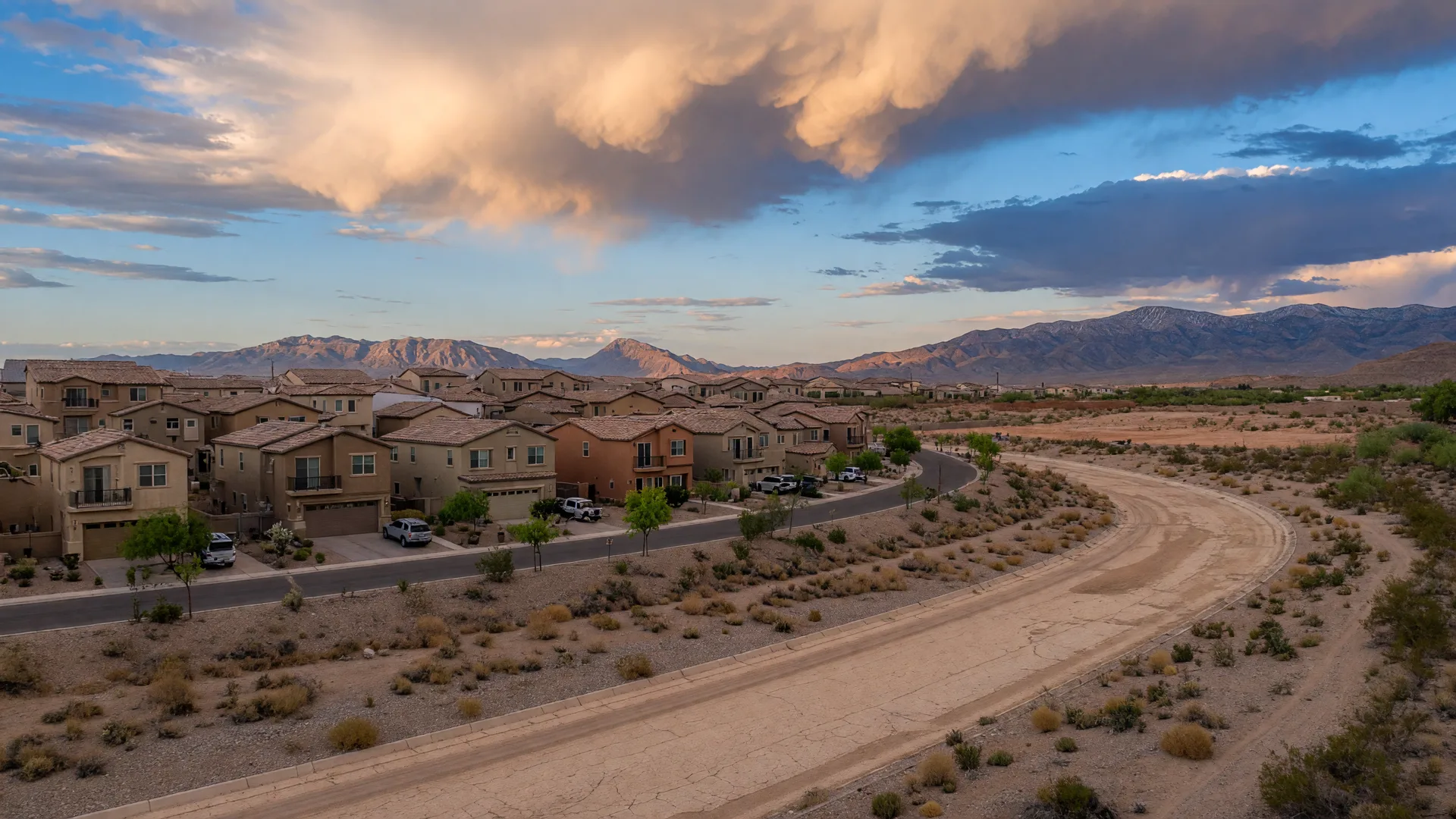 Two-story desert-tone stucco homes along a curving street in the far north Las Vegas desert, with the dry wash and mountains of the Tule Springs area beyond