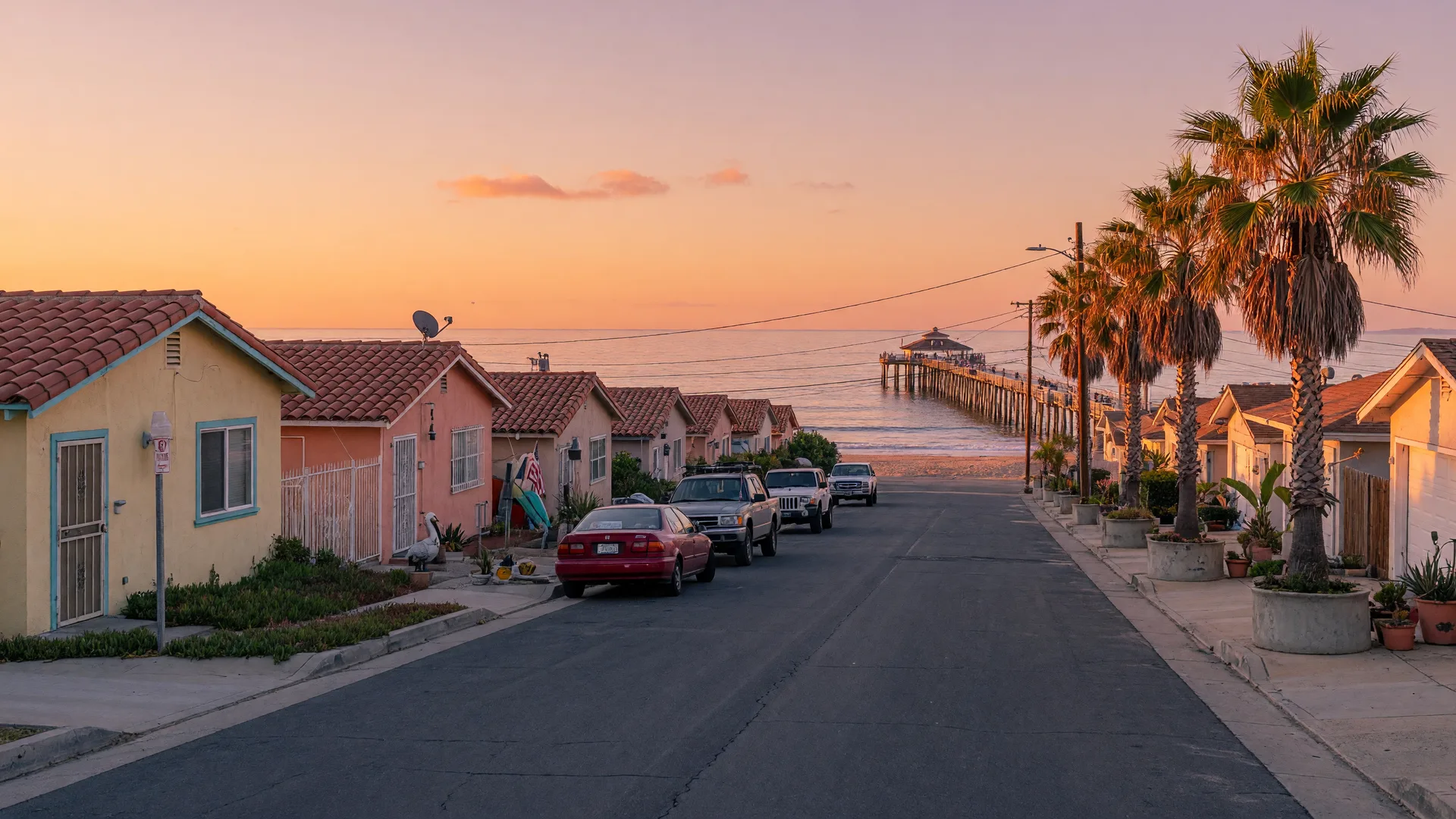 Quiet residential street in Imperial Beach, California at golden hour with low beach homes, palm trees, and the Imperial Beach Pier in the distance