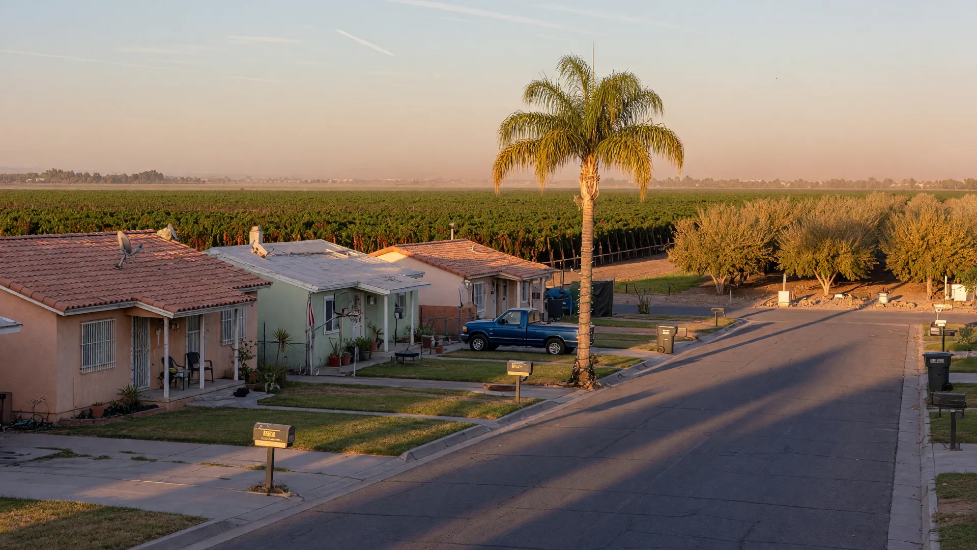 A quiet residential street in Kerman with 1990s stucco homes and farmland at the edge of town
