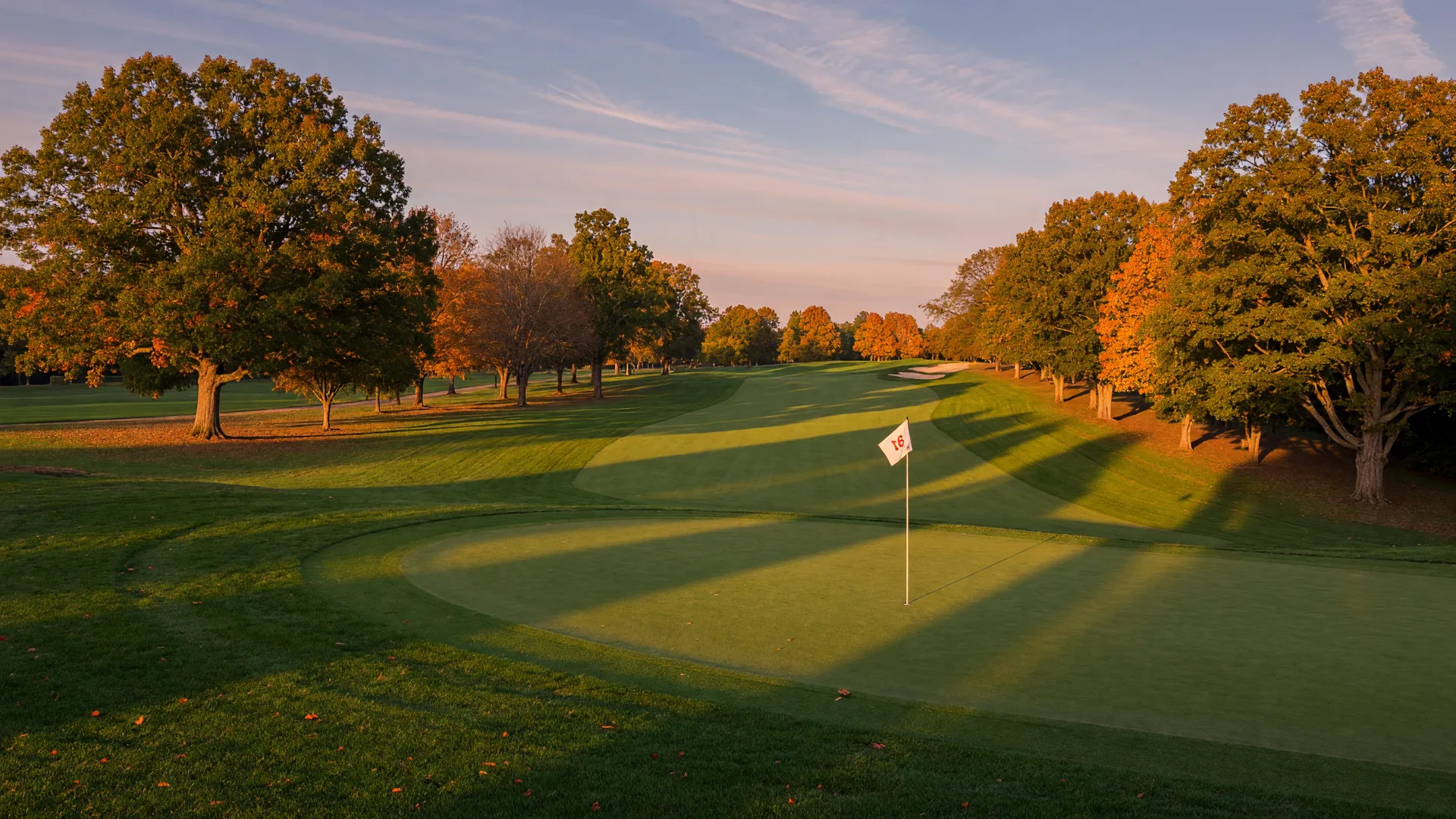 A Georgia golf course at golden hour with rolling fairways, putting greens, and mature trees showing early autumn color