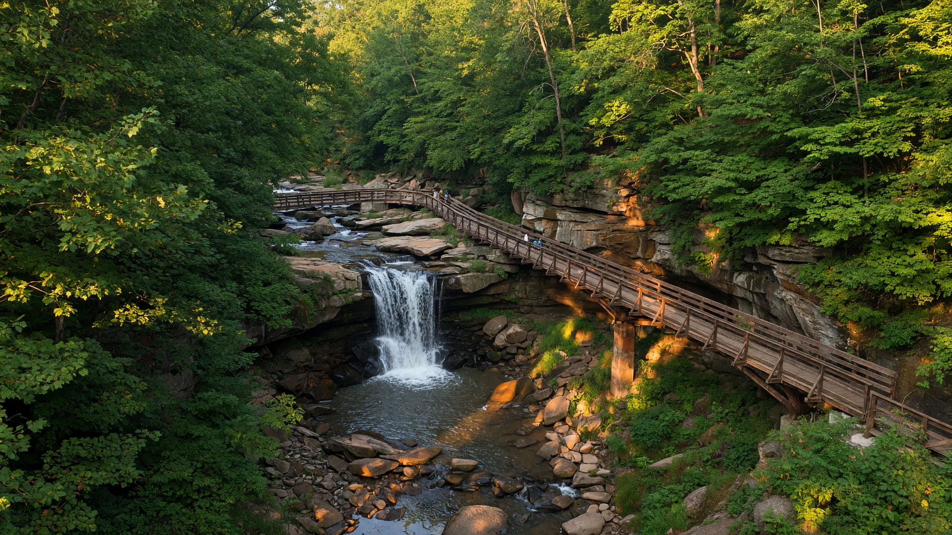 Cascade Park in Elyria, Ohio featuring a scenic waterfall and sandstone gorge with a wooden pedestrian bridge on a sunny summer afternoon