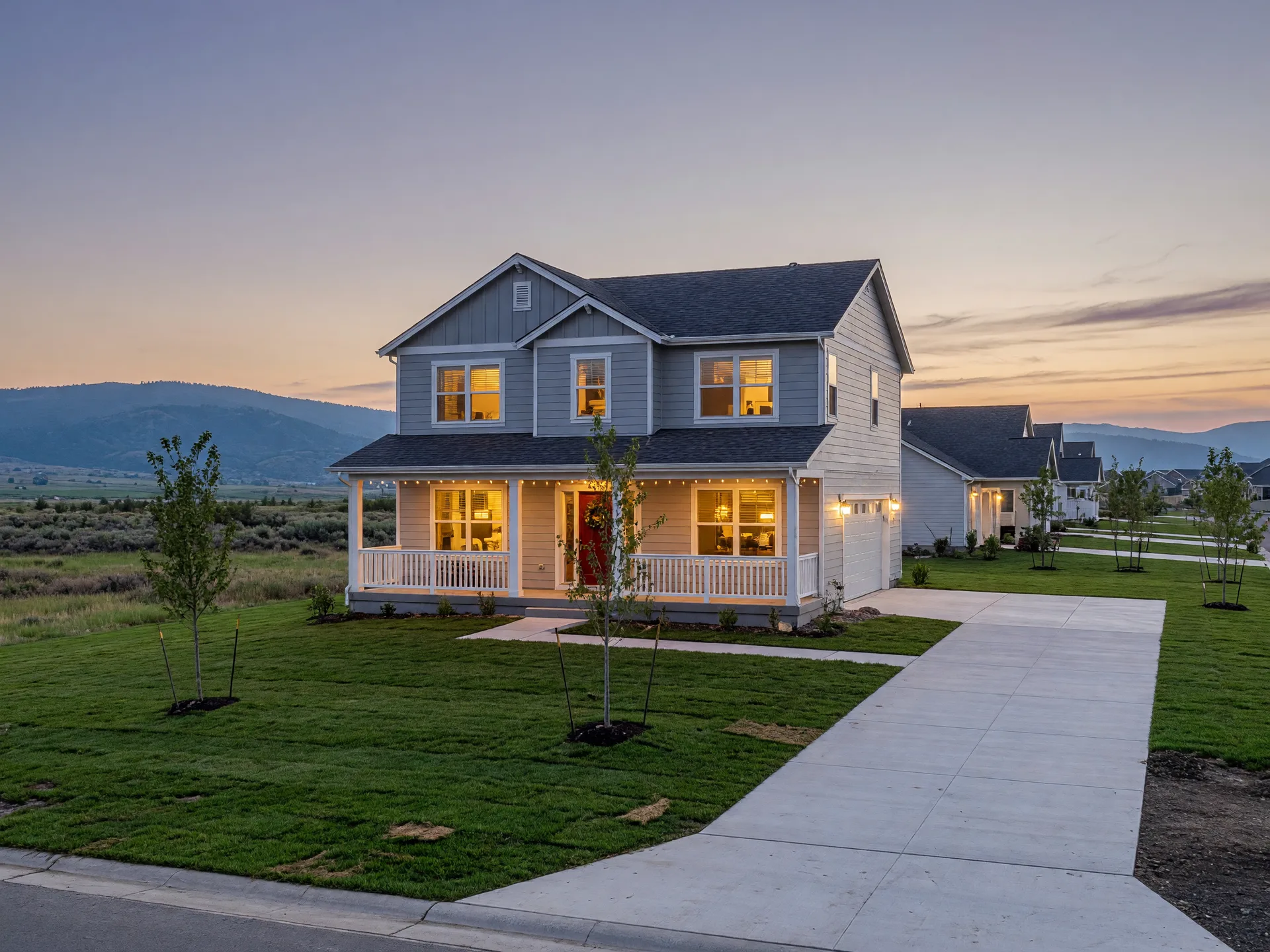 A new Idaho cul-de-sac at dusk with warm porch lights glowing from the homes