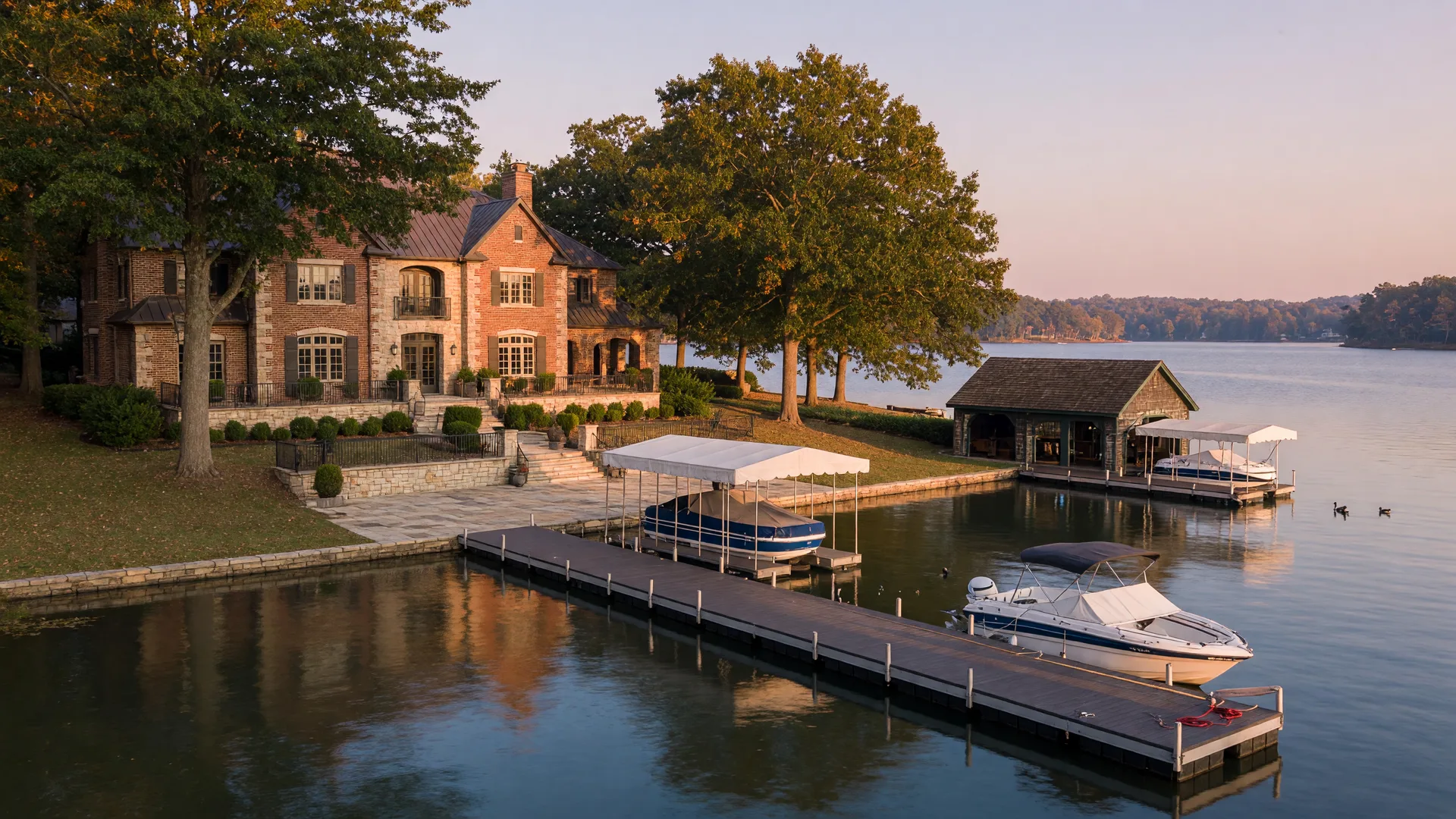 Luxury brick and stone waterfront estate on Lake Norman in early autumn with a private composite dock, covered boat lift, and boathouse, warm golden light on the water