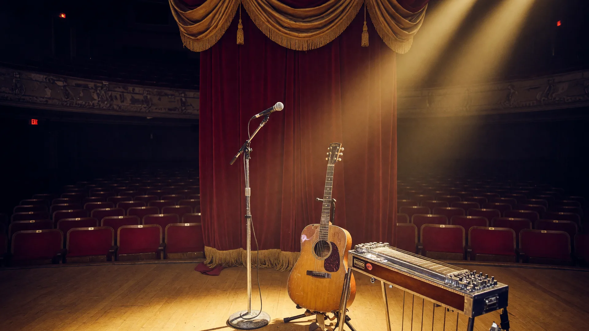 A classic country concert stage in a vintage Texas auditorium with golden spotlights, a microphone, an acoustic guitar, and a pedal steel guitar before deep red curtains
