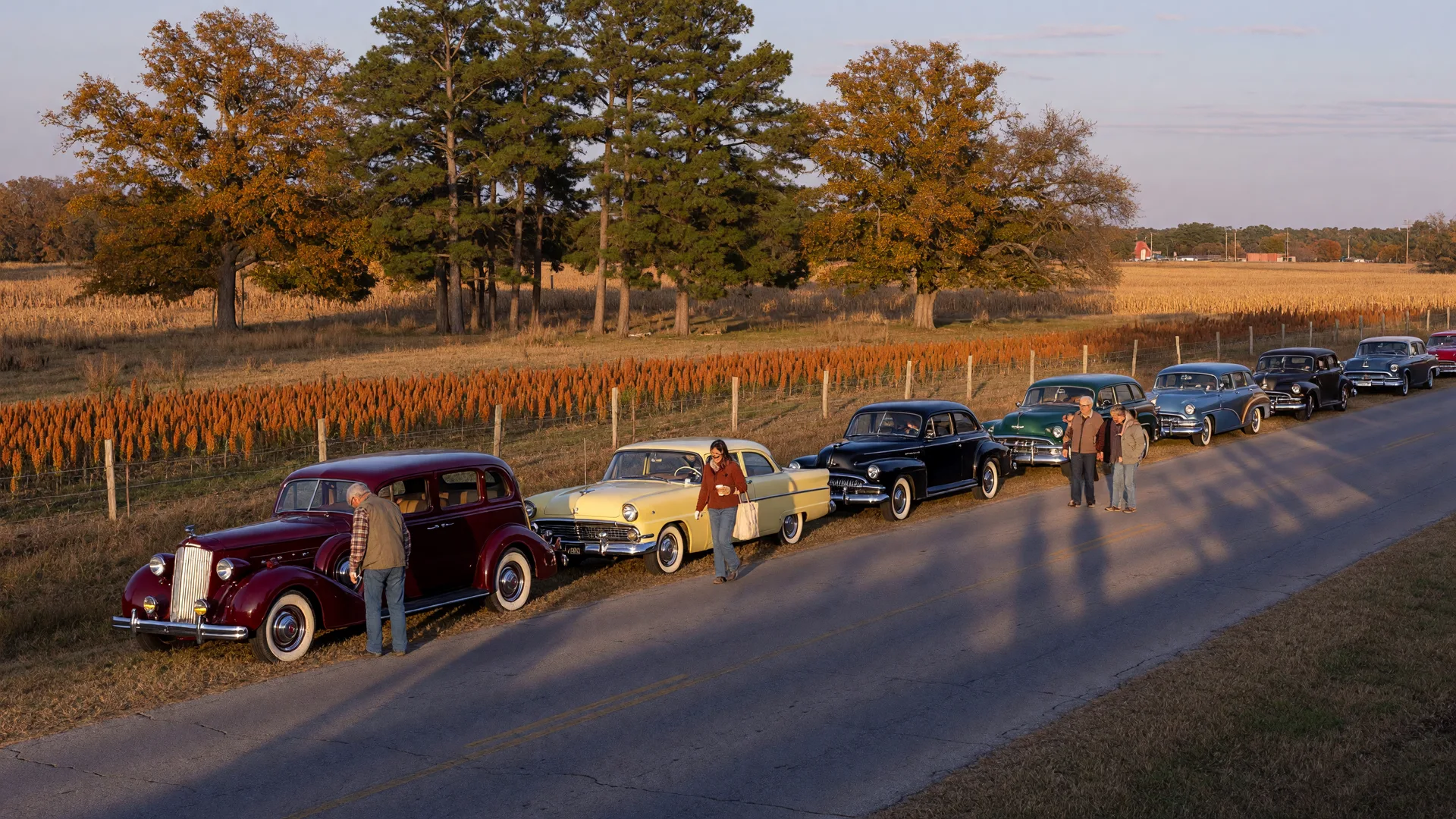 Classic and antique automobiles lined up on a quiet two-lane country road in rural Northeast Texas under golden fall light
