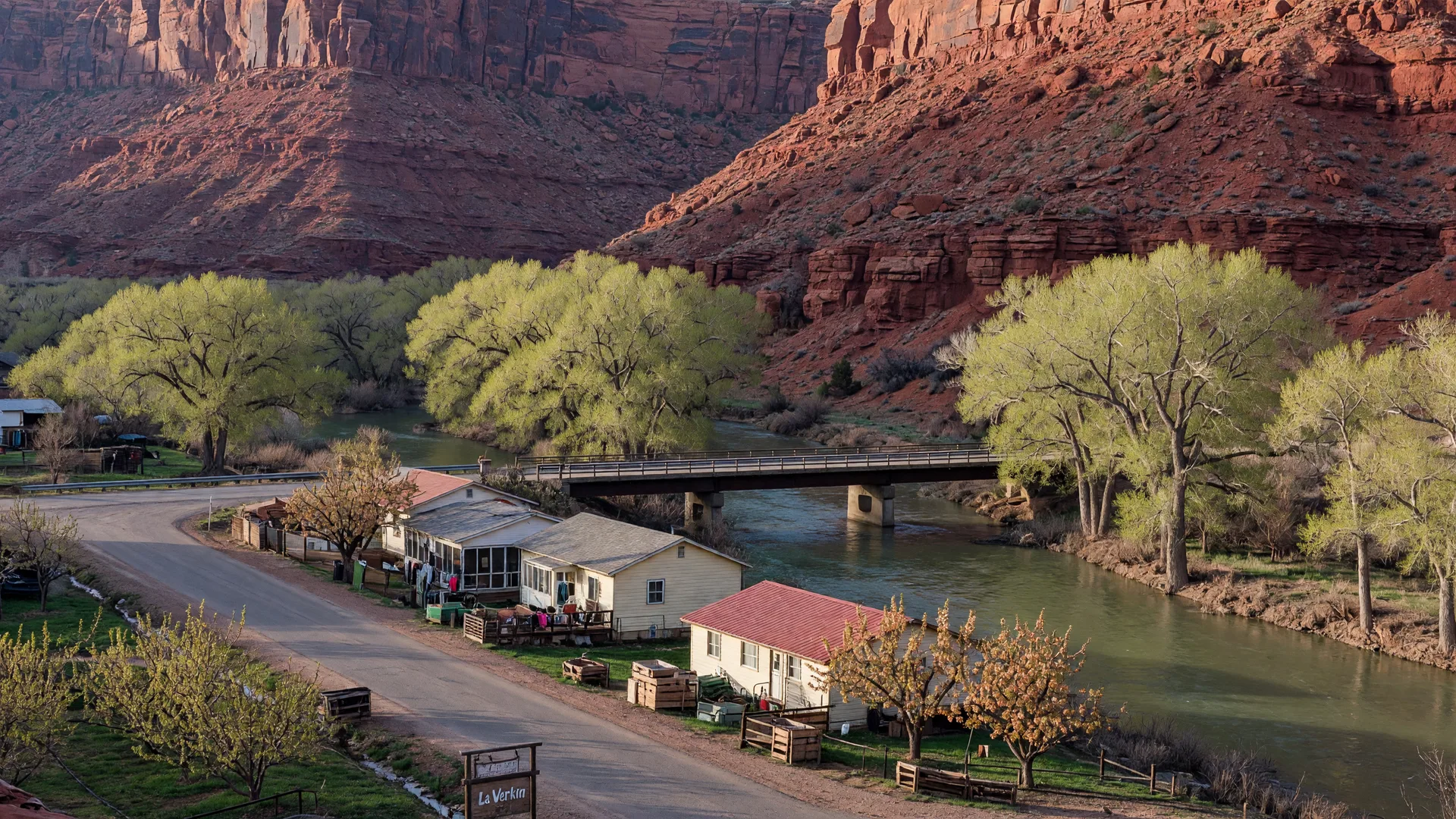 AI-rendered concept image of the Virgin River bridge and rural homes of La Verkin with red sandstone cliffs behind the town
