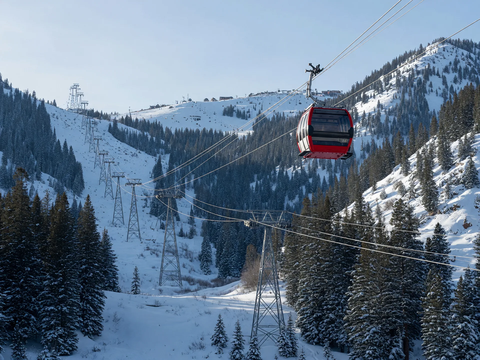 A tricable gondola cabin crossing high above a snowy alpine valley with support towers ascending toward distant ski resorts