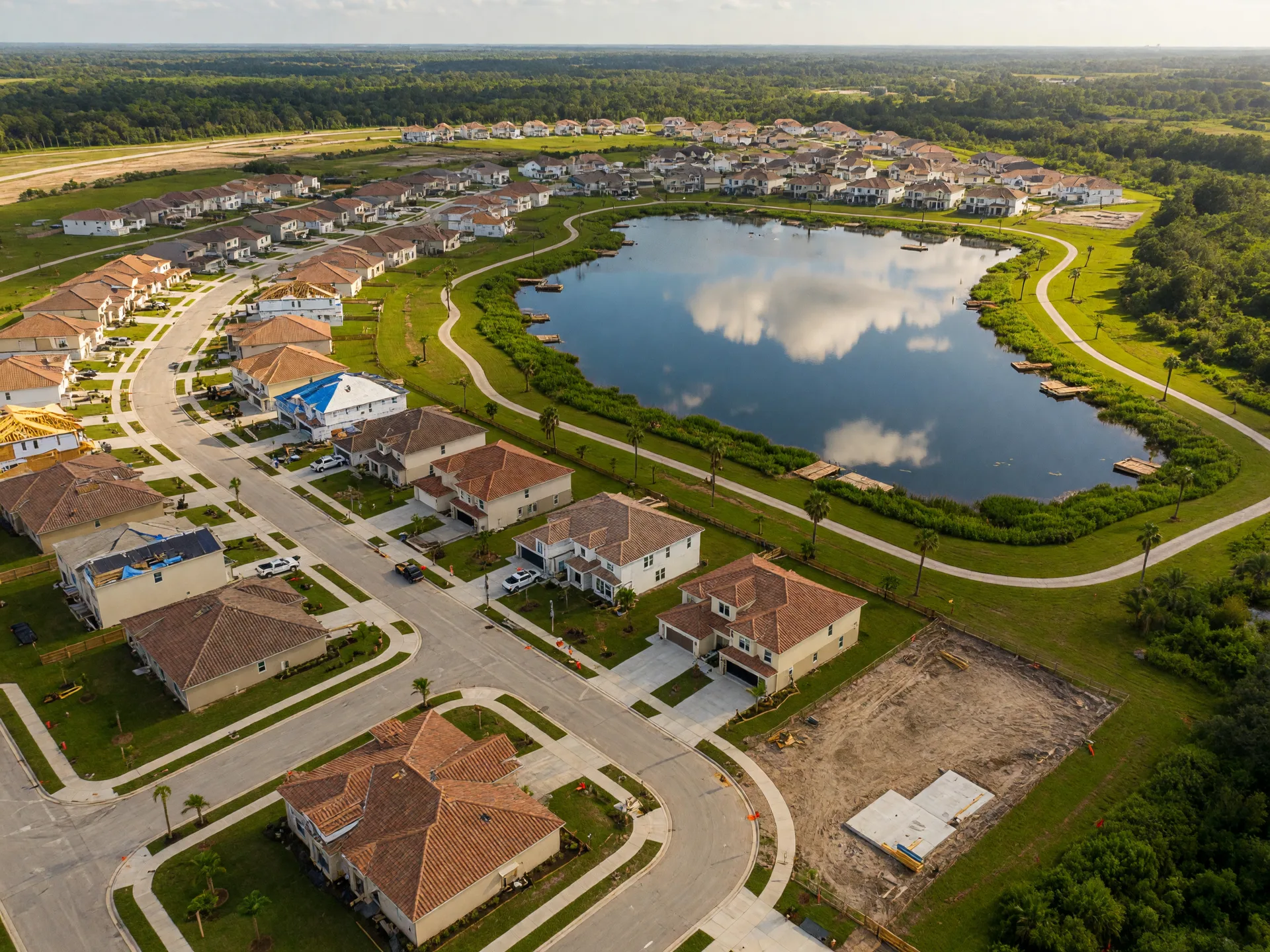 Aerial view of a new Florida residential community taking shape, with a central lake, newly paved streets, homes in various stages of construction, and green preserve areas