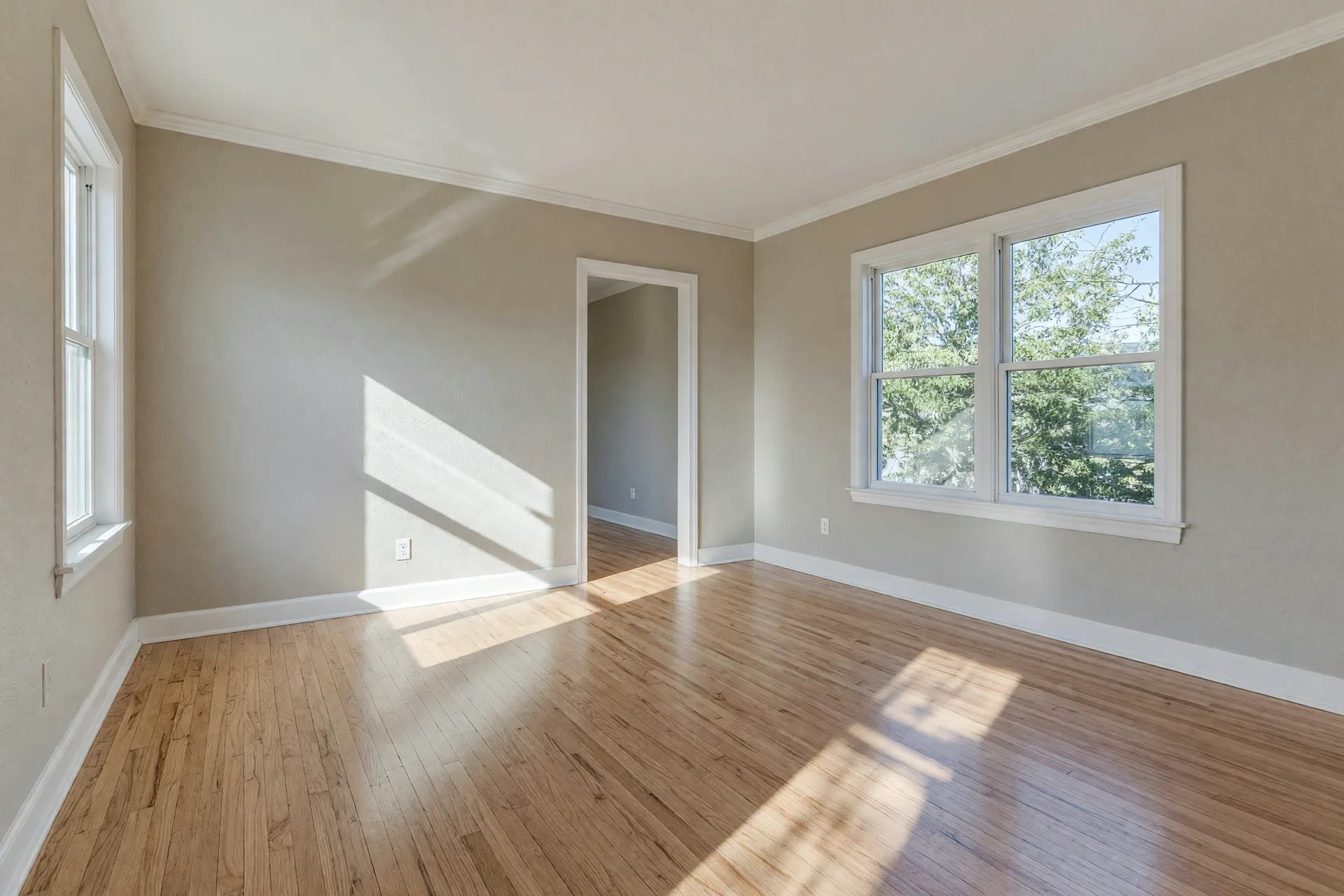 Blank empty room with beige walls and hardwood floors, waiting to be staged